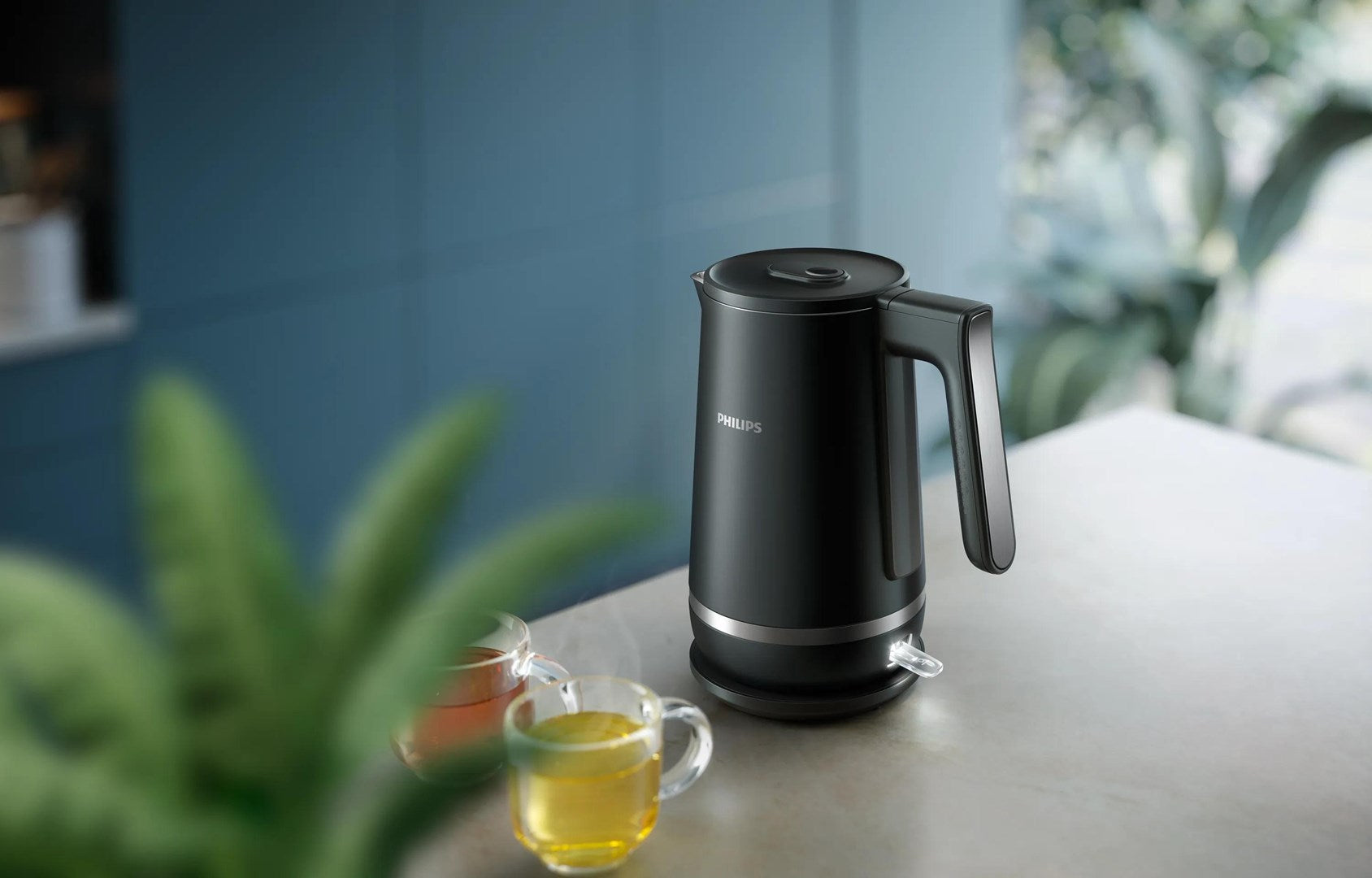 Un hervidor eléctrico Philips negro se encuentra en la encimera de una cocina junto a dos tazas de té.