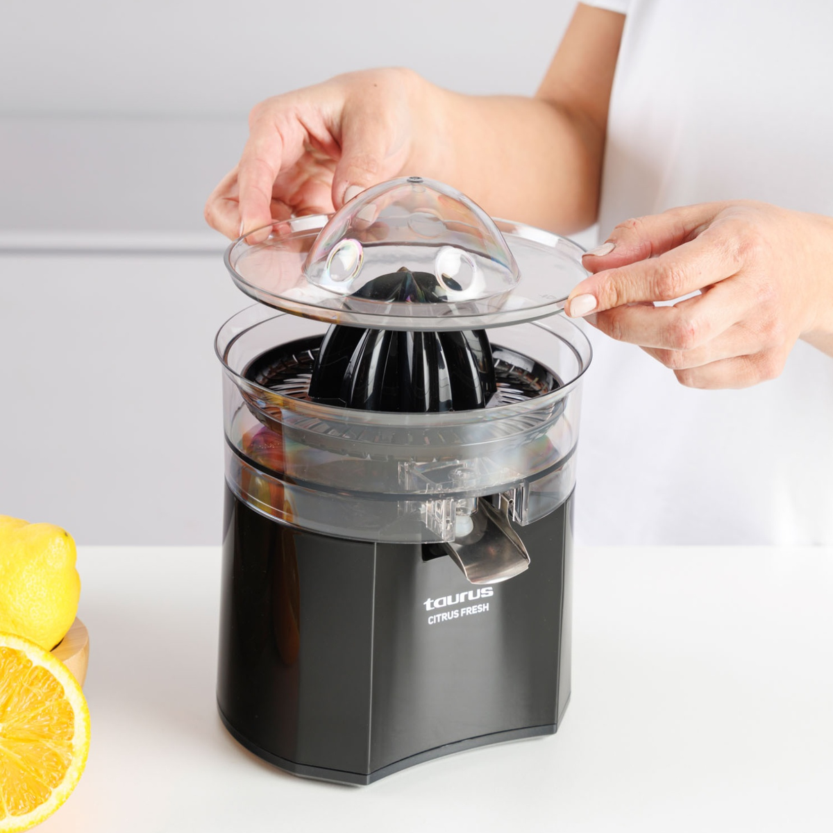 Una persona colocando la tapa transparente en un exprimidor negro Taurus Citrus Fresh.