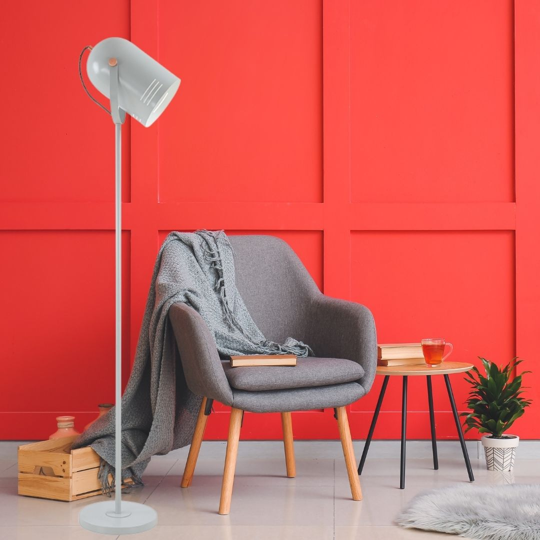 Un sillón gris con una manta, una lámpara alta y una mesita ante una pared roja.