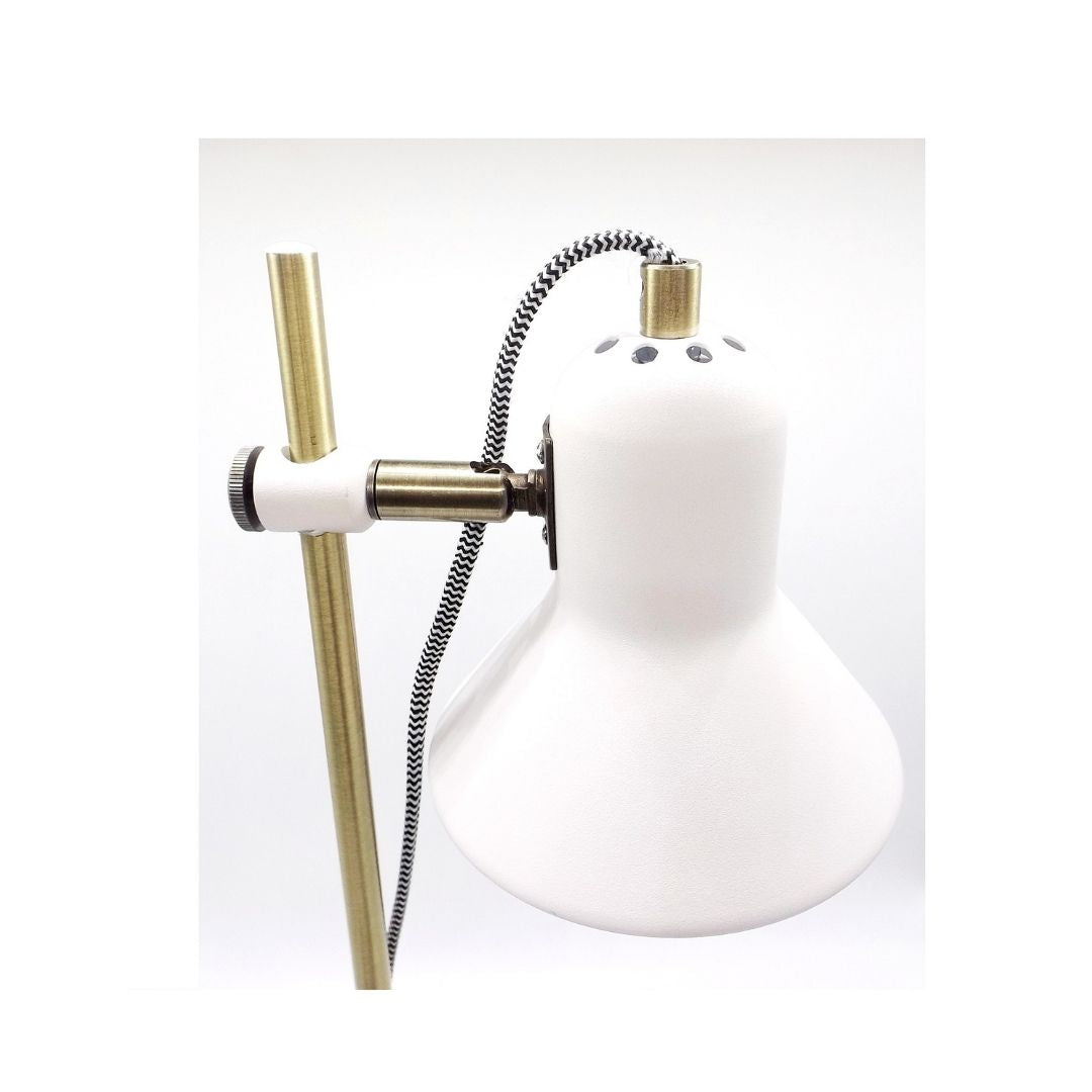 Una lámpara de escritorio blanca con soporte de latón y cable estampado en blanco y negro sobre fondo blanco.