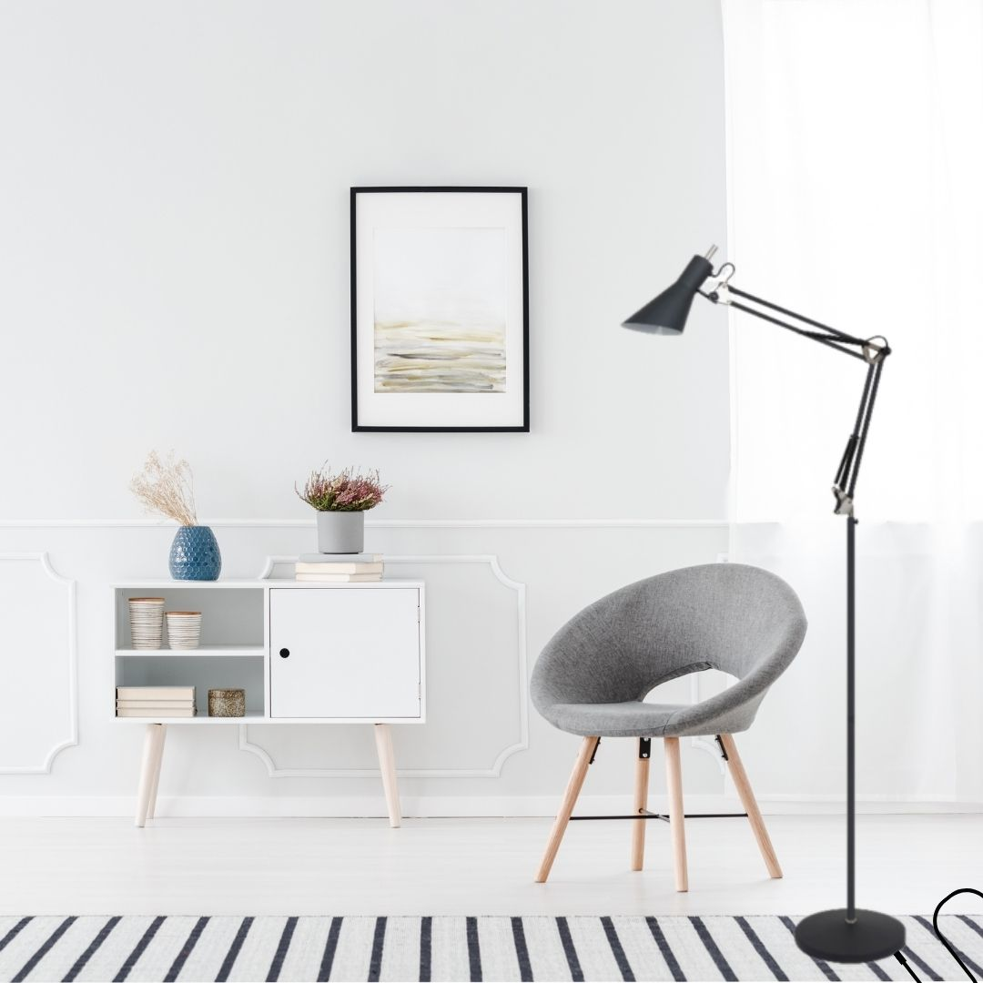 Habitación luminosa con un sillón gris, mueble blanco, lámpara de pie negra y cuadro en la pared.