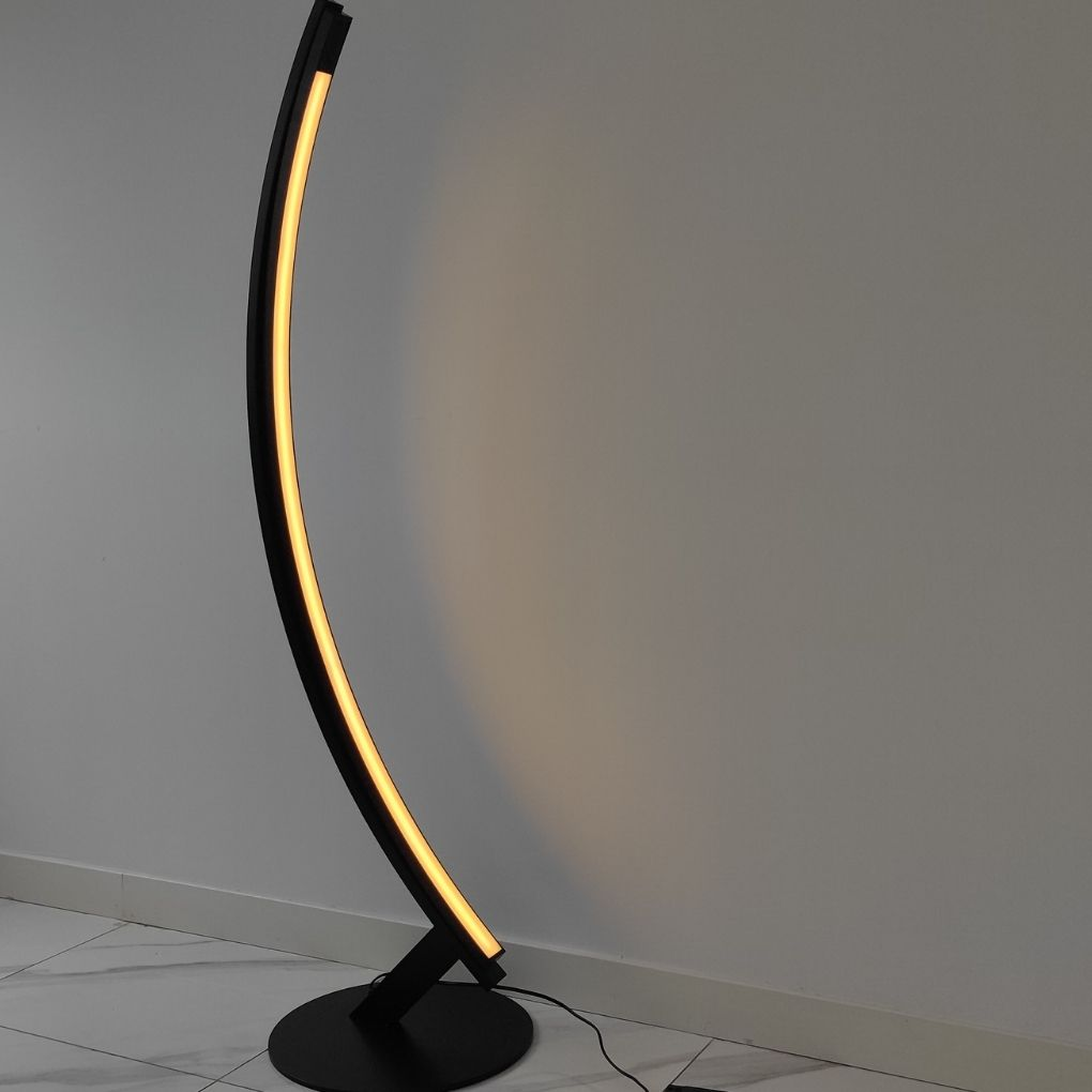 Una lámpara de pie negra curvada con luz amarilla cálida se encuentra en un suelo de baldosas blancas contra una pared gris.