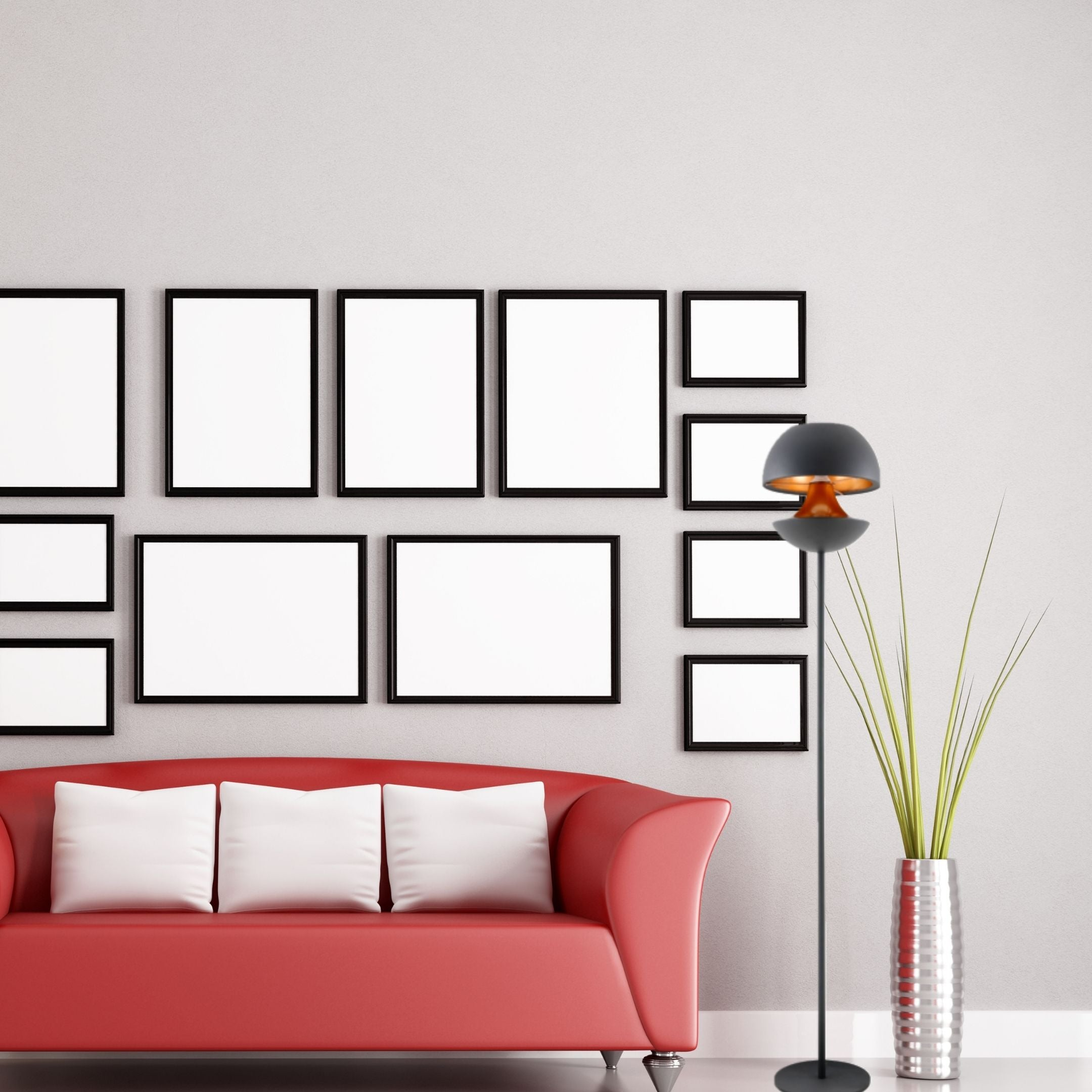 Un sofá rojo con cojines blancos, una pared de cuadros, una lámpara y una planta en un jarrón plateado.