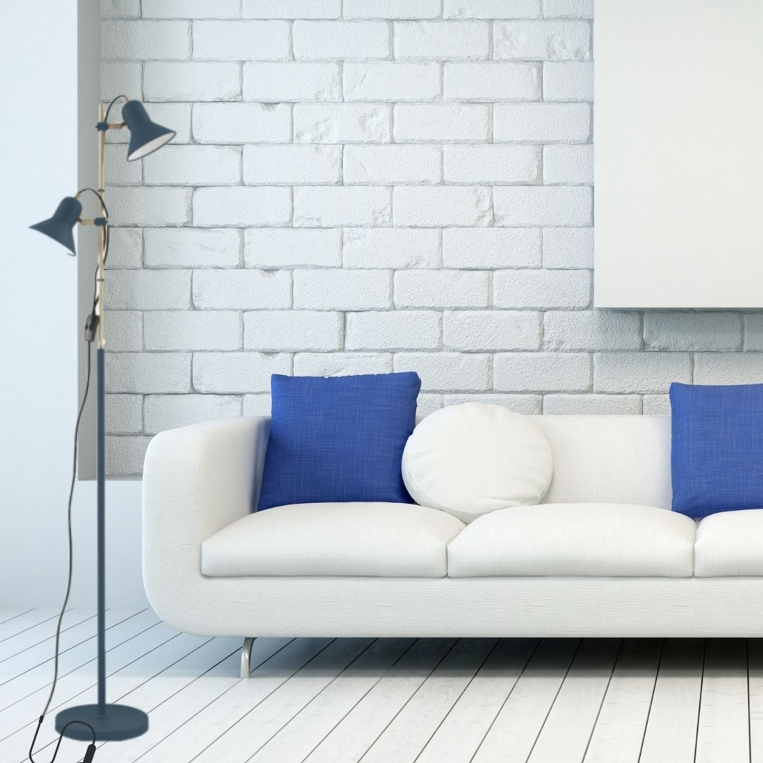 Un sofá blanco con cojines azules contra una pared de ladrillo blanco, con una lámpara de pie cerca.