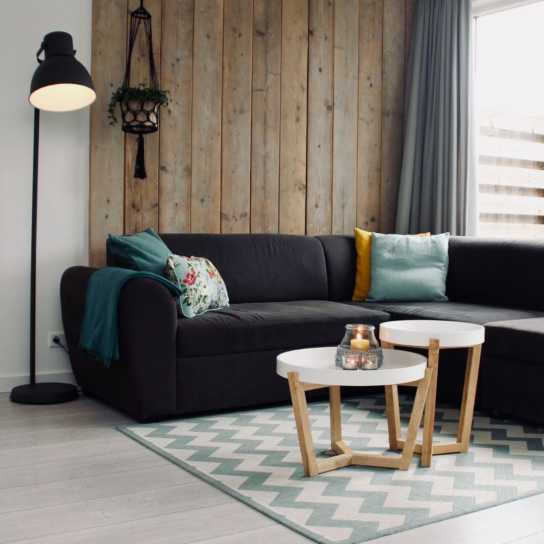 Sala de estar acogedora con un sofá seccional oscuro, pared de madera, dos mesas de centro y lámpara.