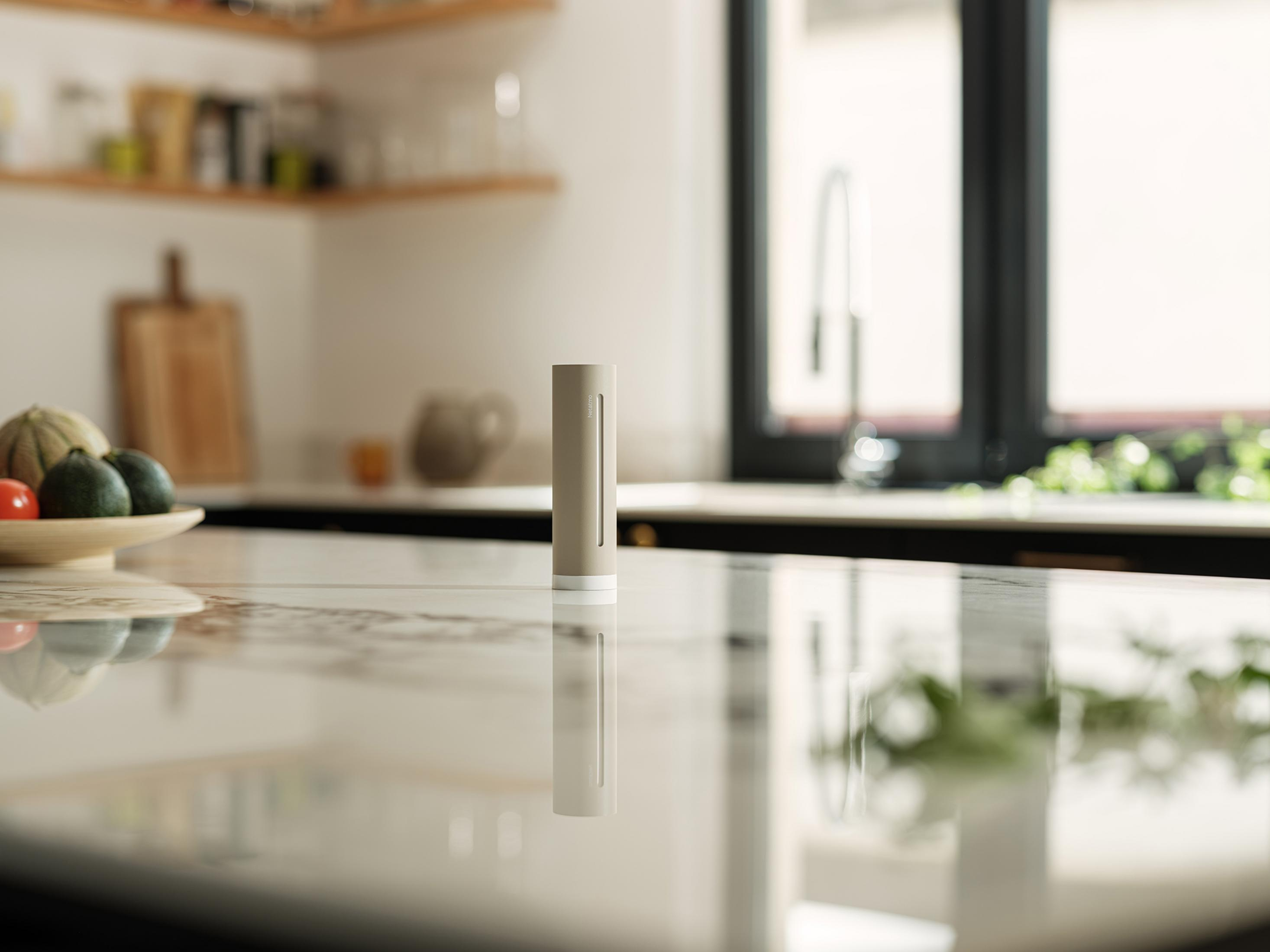 Un sensor beige sobre una encimera de cocina brillante, con una ventana y estantes al fondo.