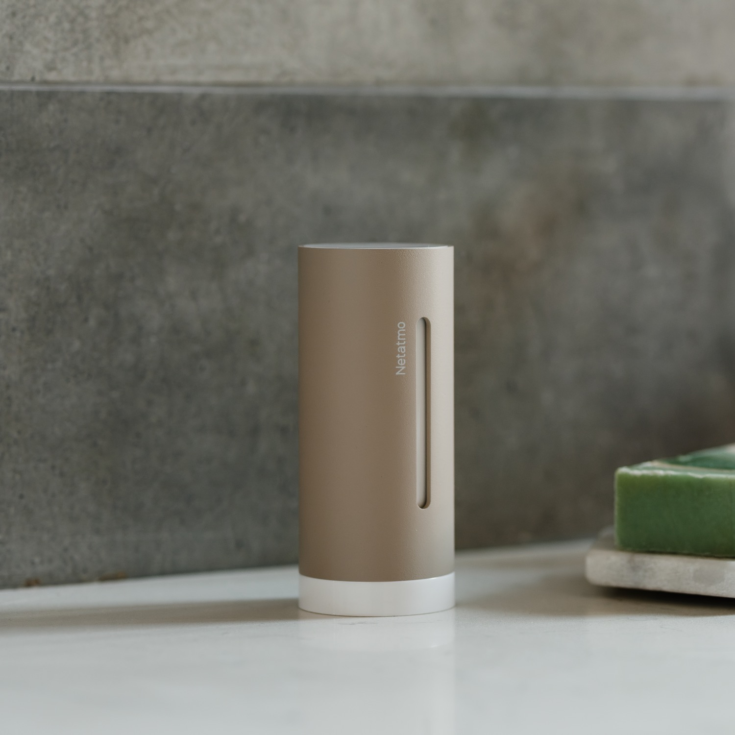 Un sensor Netatmo cilíndrico de color beige con base blanca se encuentra sobre una superficie blanca.