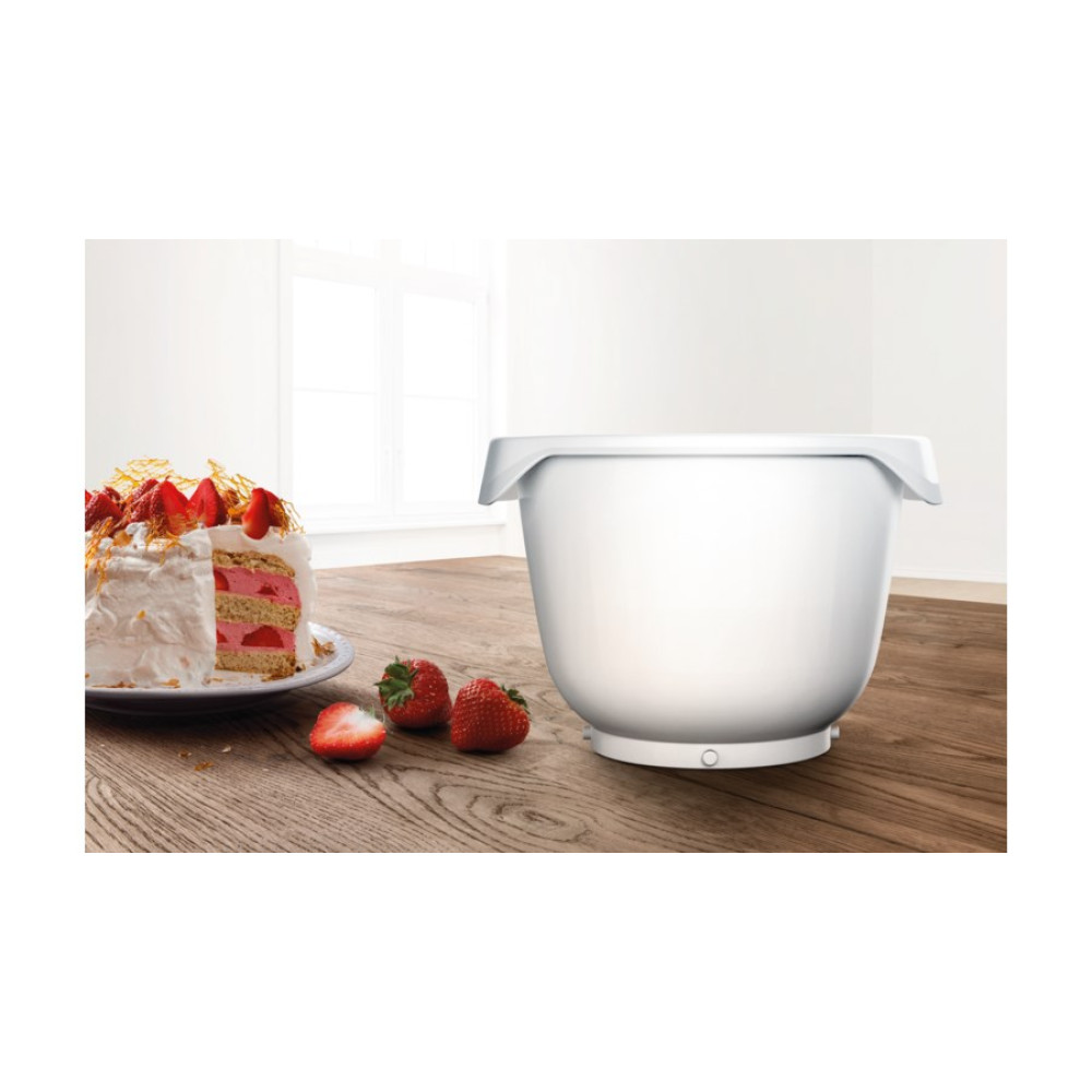 Un bol mezclador blanco sobre una mesa de madera junto a un pastel de fresas y fresas frescas.
