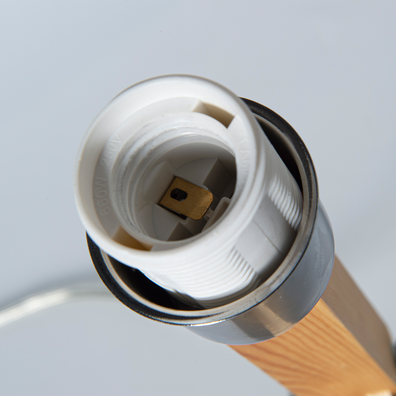Primer plano de un portalámparas blanco con contacto dorado, montado en una base de madera sobre fondo gris.