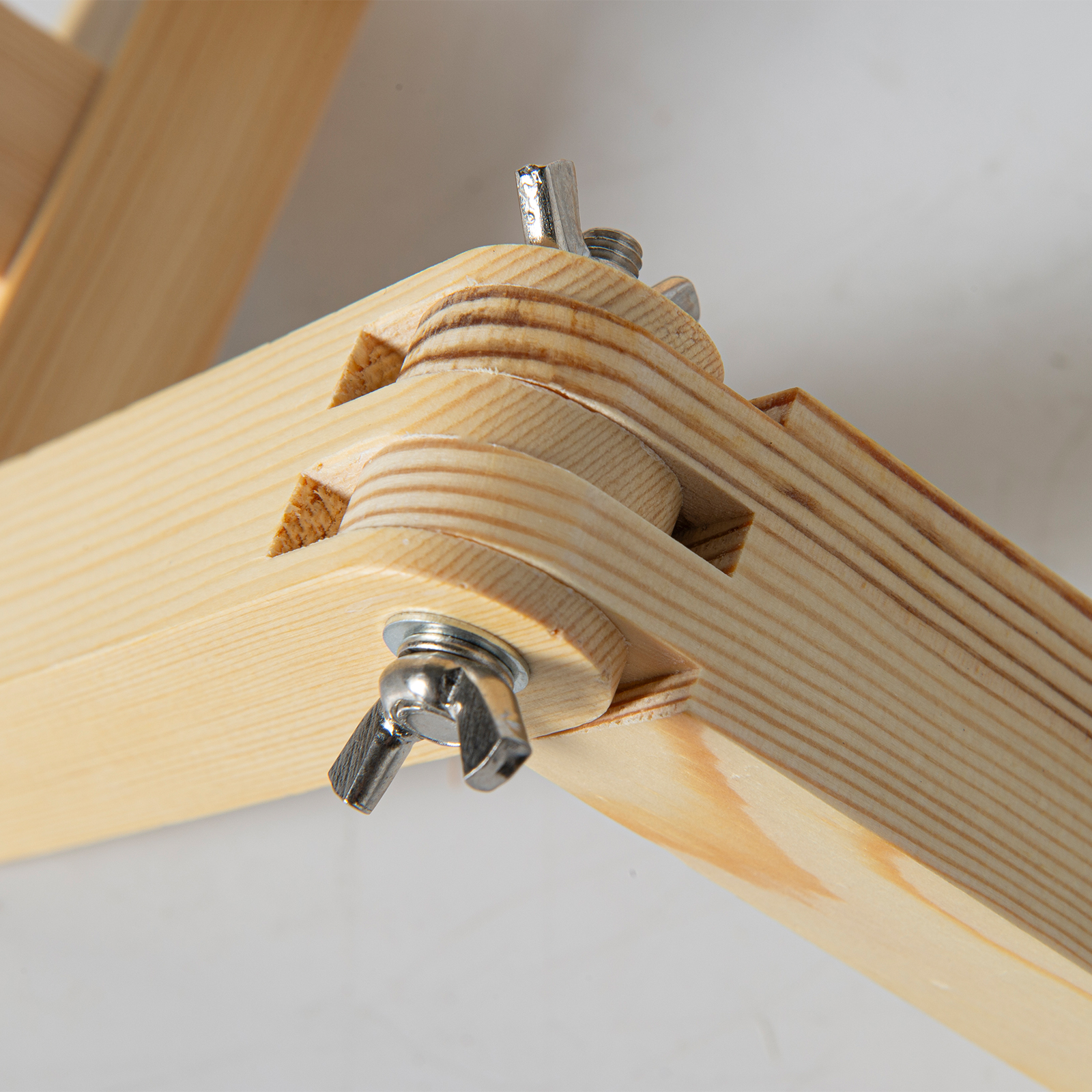 Articulación de madera con tuercas de mariposa plateadas sobre fondo claro.