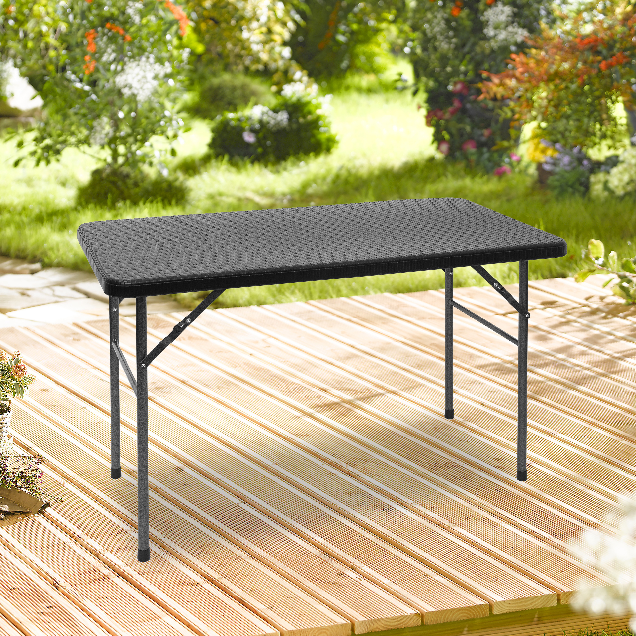 Ein schwarzer Klapptisch steht auf einer Holzterrasse vor einem grünen Garten.