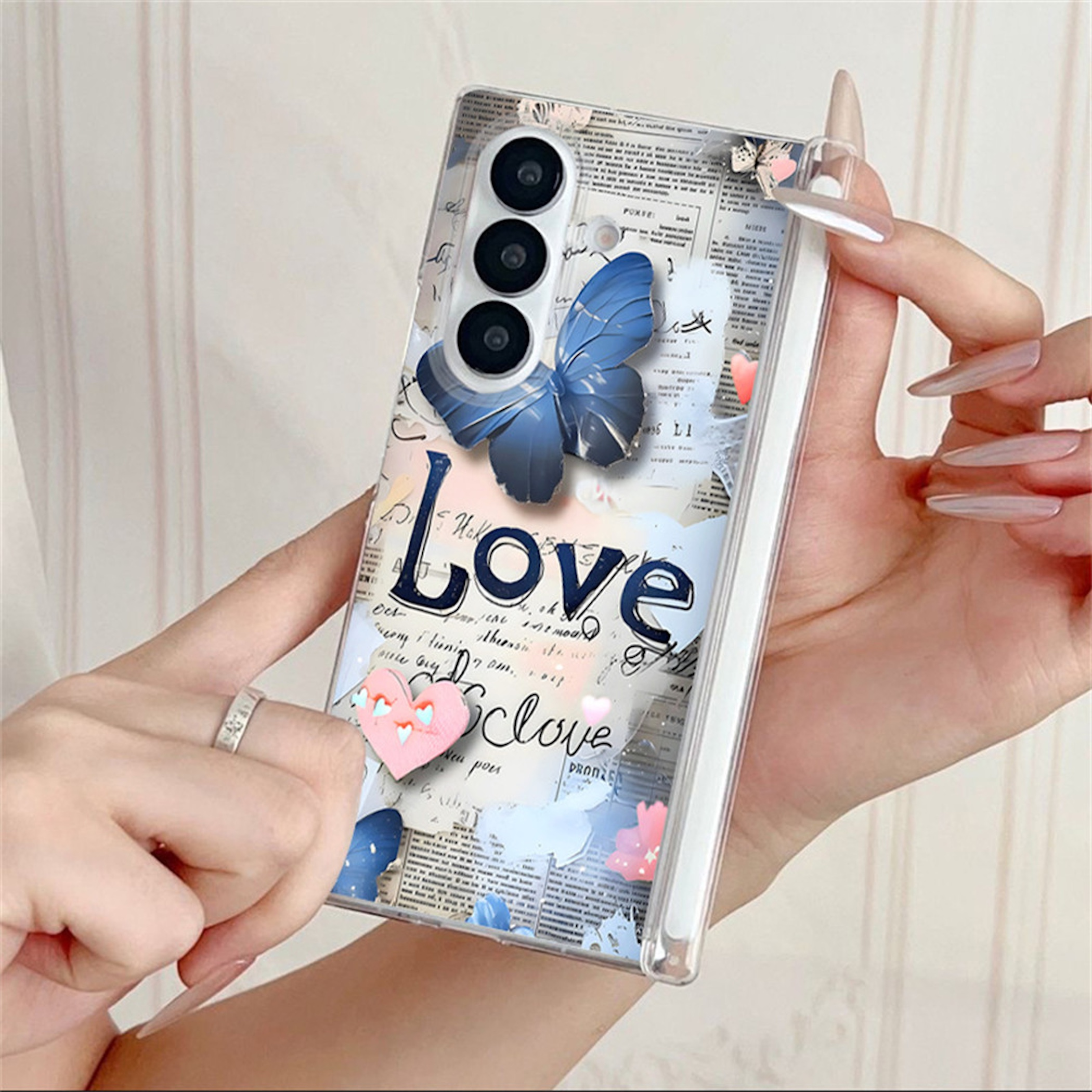 Hände halten eine Smartphone-Hülle mit blauem Schmetterling, Zeitungsmotiv und dem Schriftzug Love.