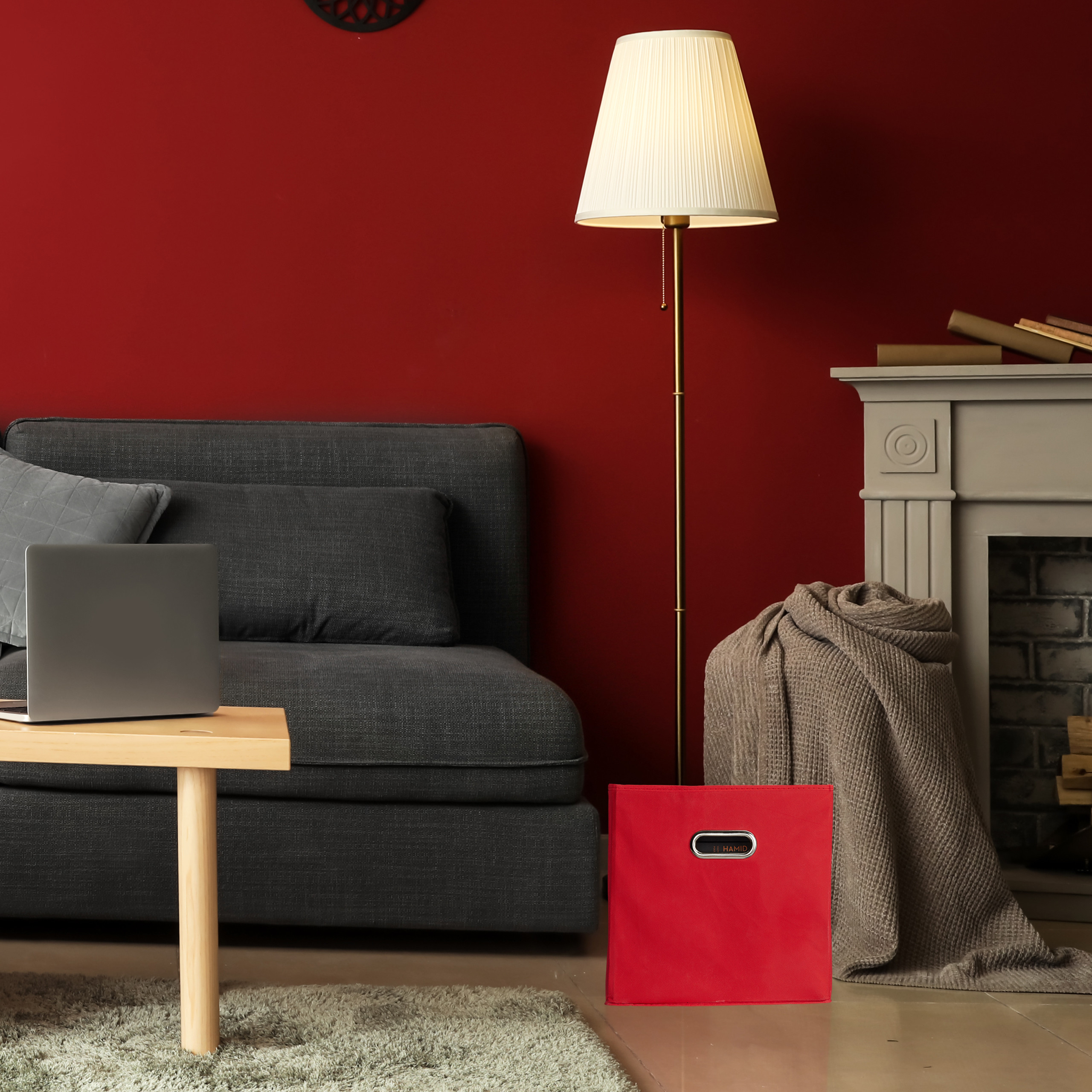 Wohnzimmer mit dunkelgrauem Sofa, roter Wand, Stehlampe und Kamin mit Decke.