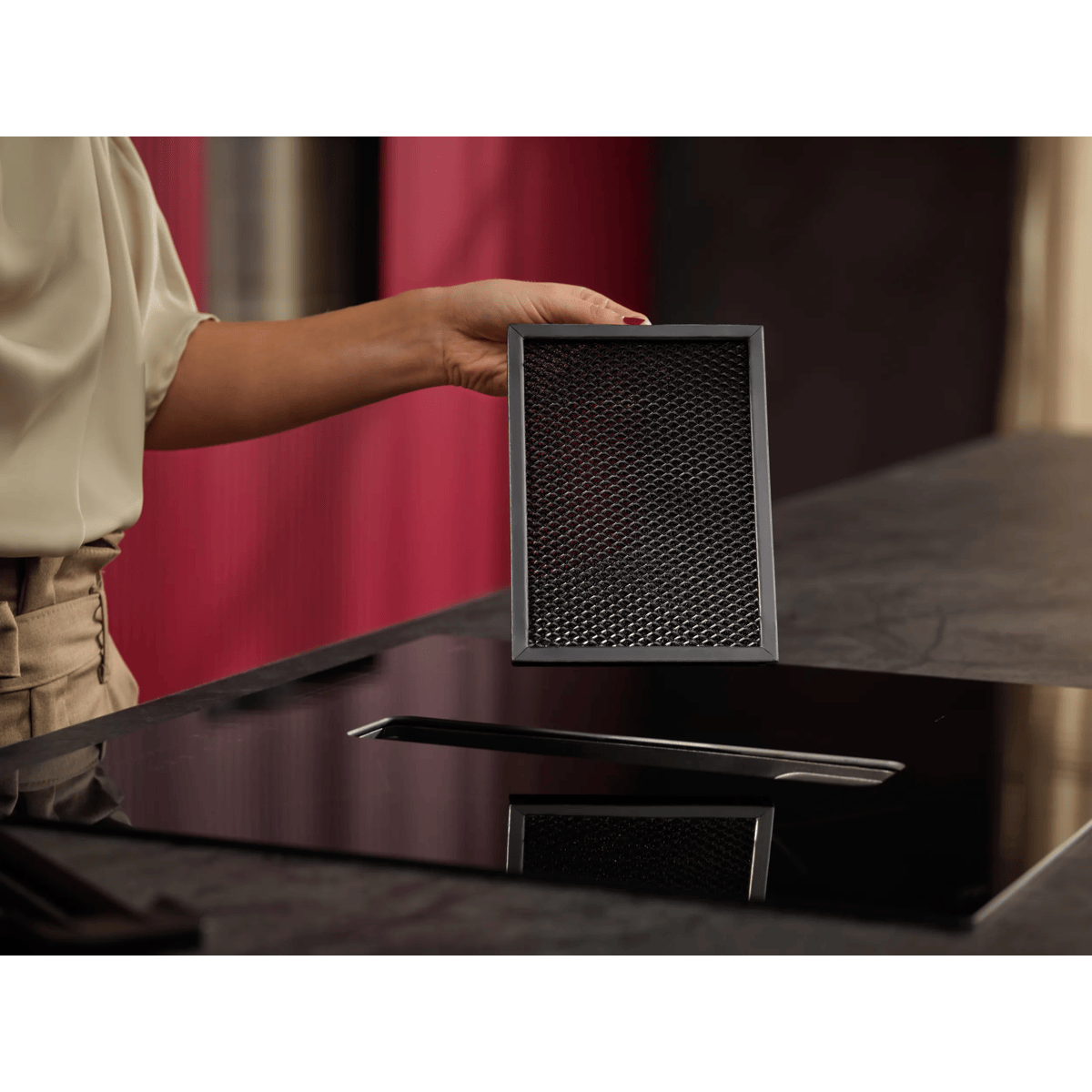 Una persona sostiene un filtro de malla rectangular negro sobre una placa de cocción de vidrio.