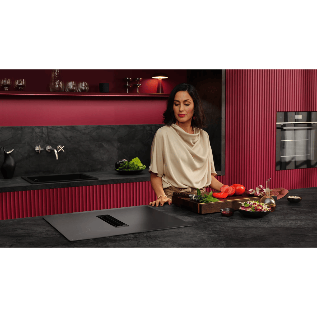 Una mujer en una cocina moderna con gabinetes rojos está frente a una placa de inducción y una encimera.