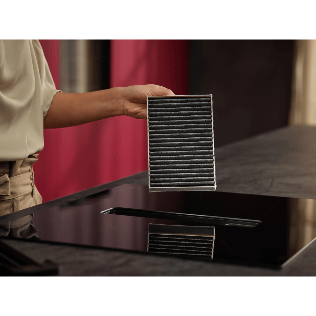 Persona sosteniendo un filtro de carbón negro rectangular sobre una placa extractora negra en la cocina.