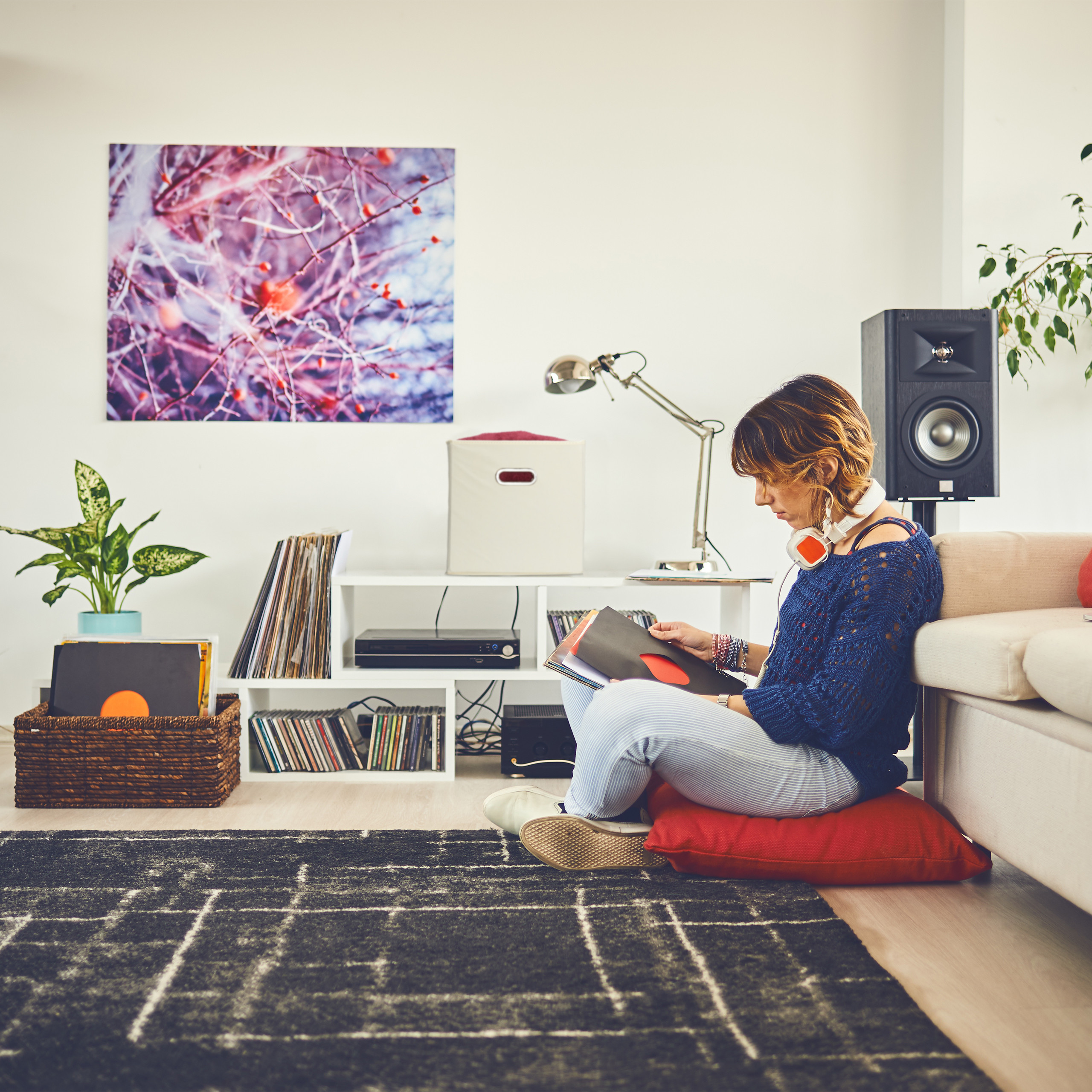 Eine Frau mit Kopfhörern sitzt auf einem roten Kissen und schaut sich in einem gemütlichen Zimmer Schallplatten an.