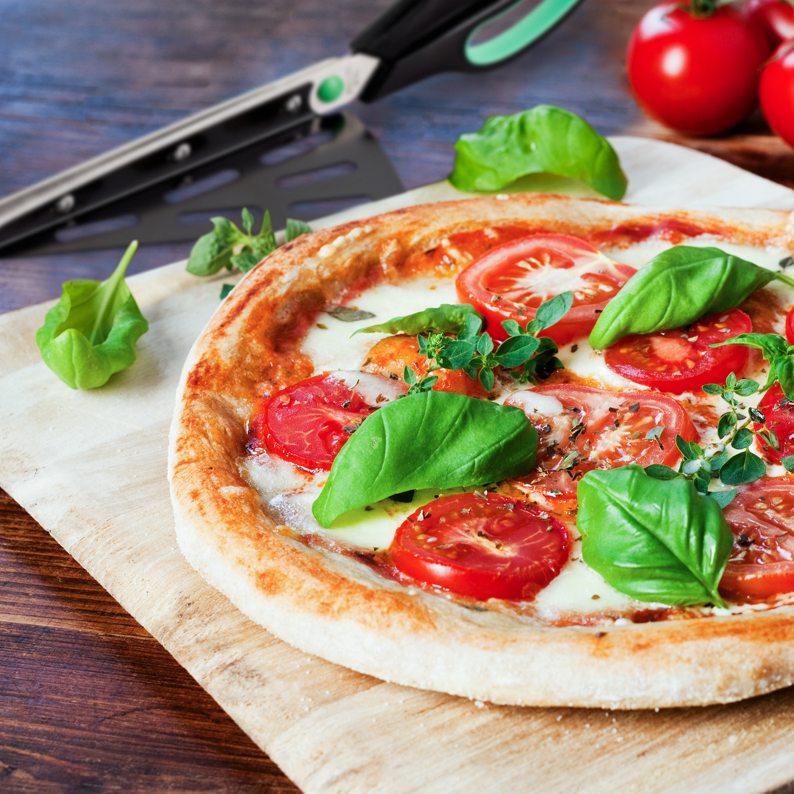 Frische Pizza mit Tomaten und Basilikum auf einem Holzbrett.