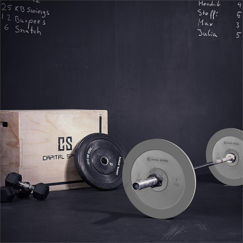Fitnessstudio-Szene mit einer Langhantel, Hantelscheiben, einer Holz-Plyobox und schwarzen Hanteln vor einer Wand.