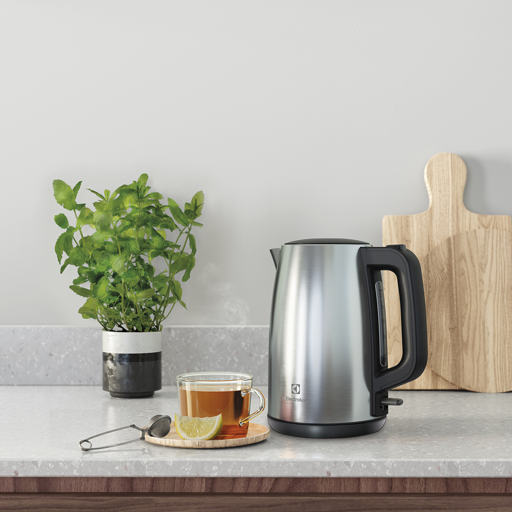 Un bollitore argentato, una tazza di tè con limone, menta fresca in vaso e un tagliere sul piano cucina.