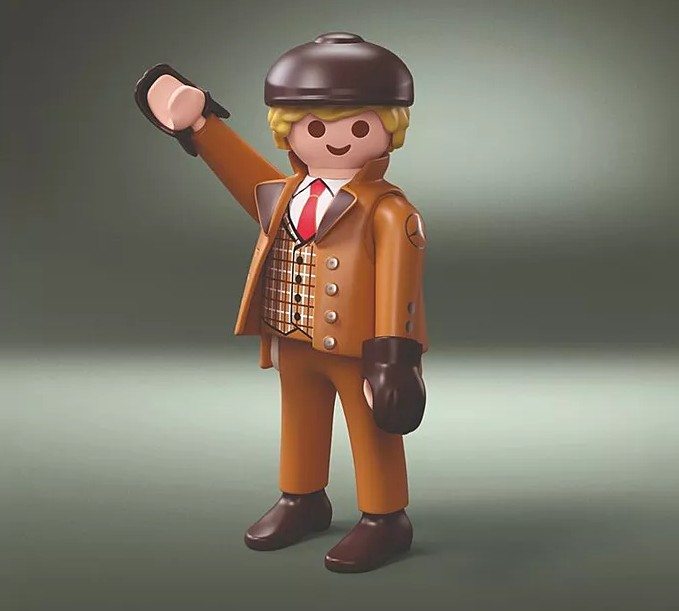 Kahverengi kabanlı, şapkalı, yelekli ve kırmızı kravatlı Playmobil figürü sağ elini kaldırıyor.