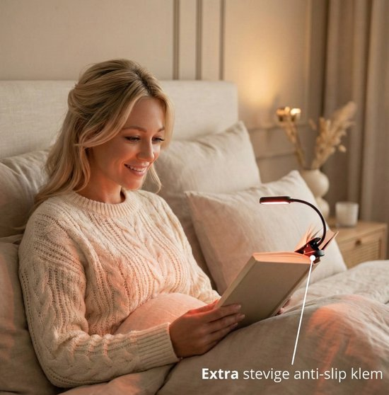 Donna bionda legge un libro a letto con una piccola lampada a clip.