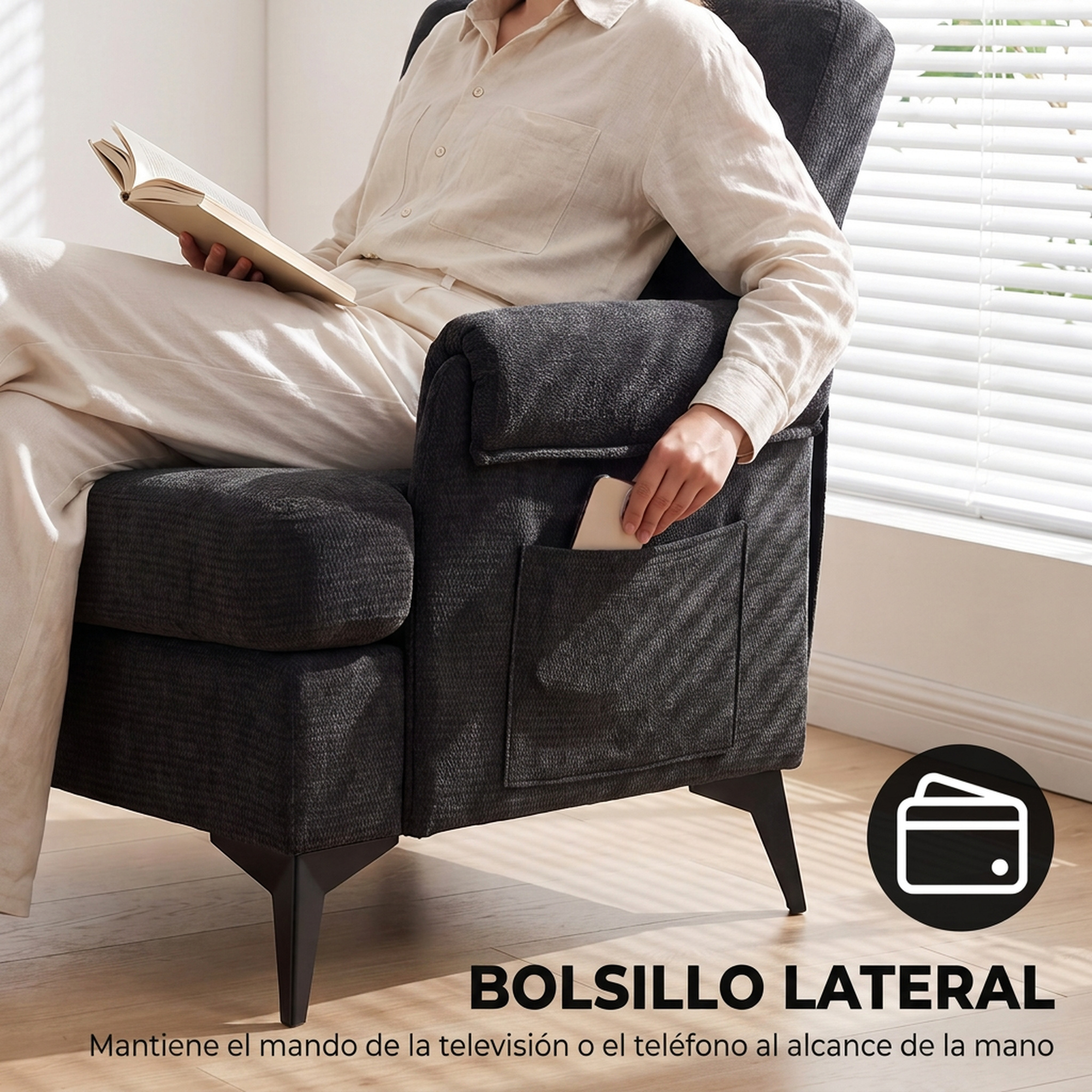 Una persona lee un libro en un sillón gris oscuro con un teléfono en el bolsillo lateral.