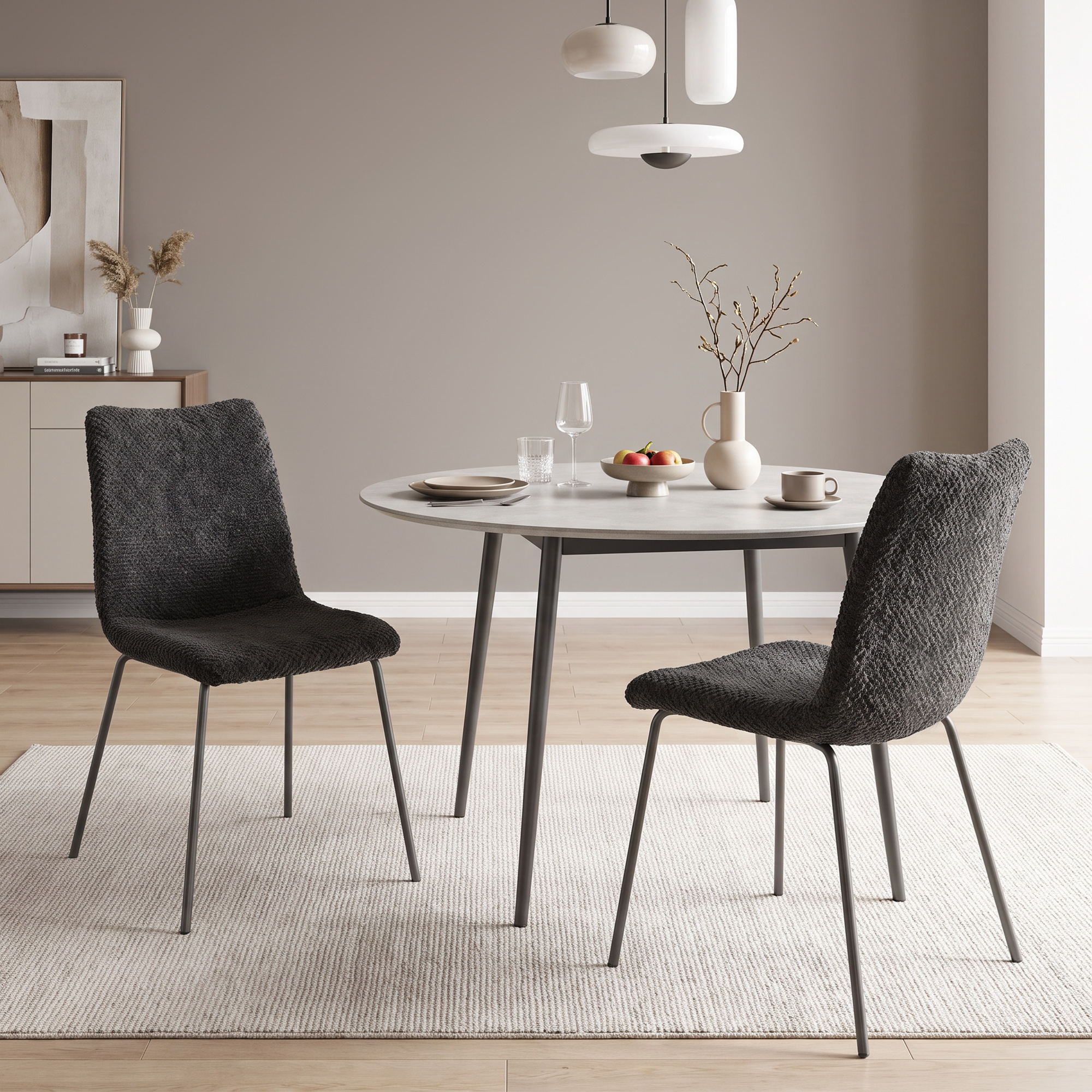 Un comedor moderno con dos sillas oscuras texturizadas, mesa redonda, vajilla y luces colgantes en un cuarto neutro.