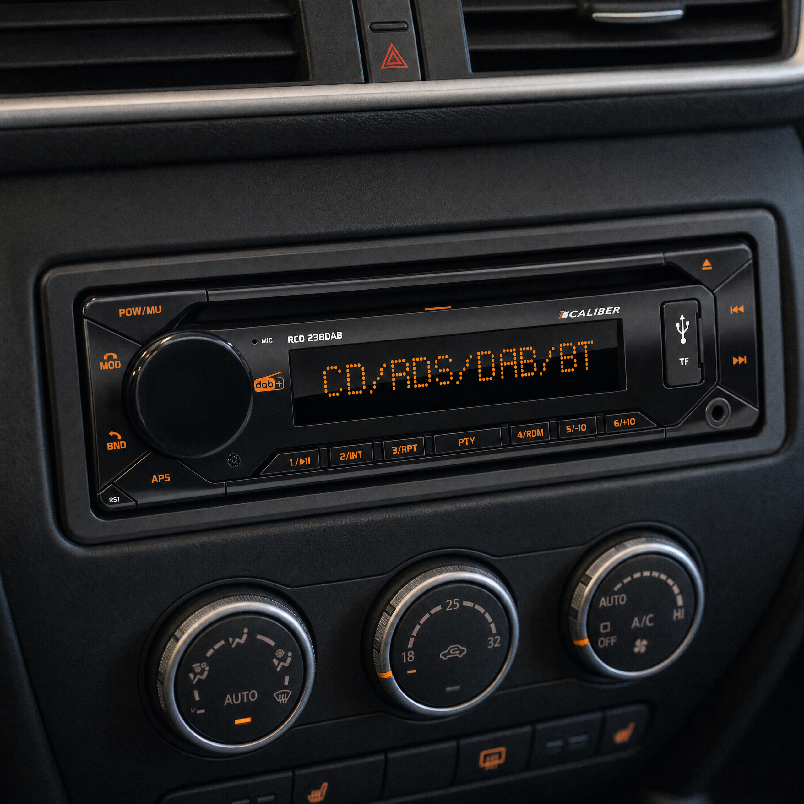 Car interior featuring a Caliber RCD 238DAB car radio with an orange display and three round climate knobs below.