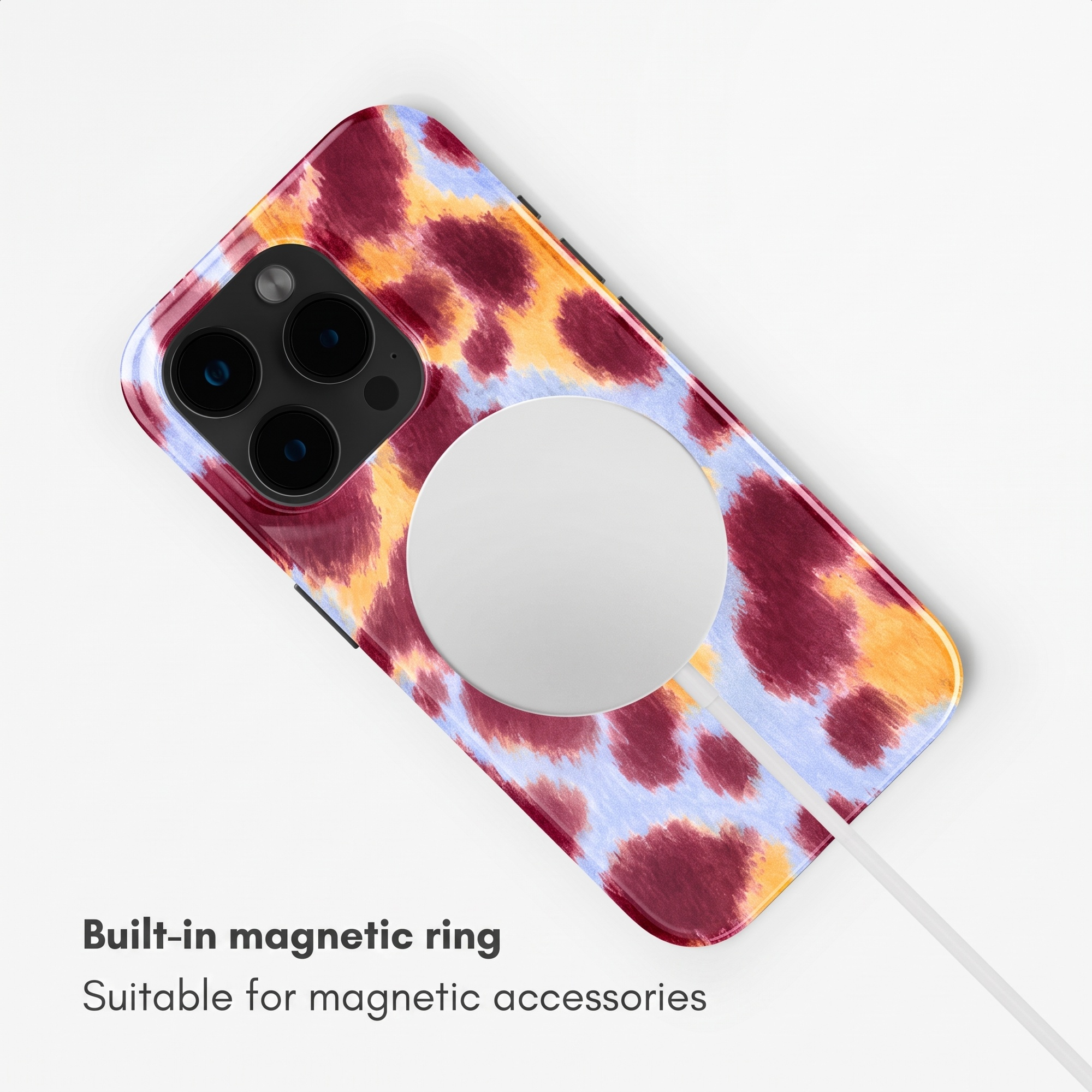 Smartphone in buntem Kuhfell-Muster mit weißem MagSafe-Ladegerät auf weißem Grund.
