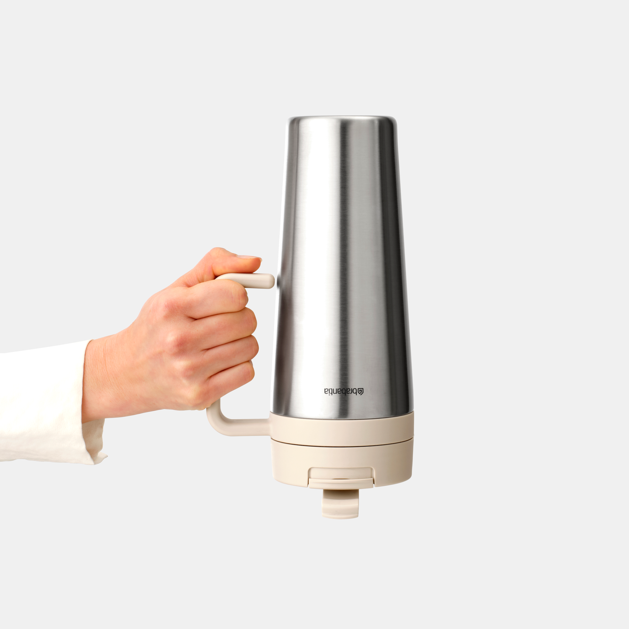 Een hand houdt een RVS reismok vast met een beige basis en handvat tegen een lichte achtergrond.