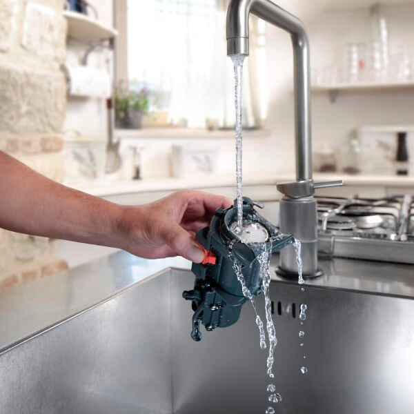 Una mano lava un pequeño dispositivo mecánico bajo el agua corriente de un grifo de cocina.