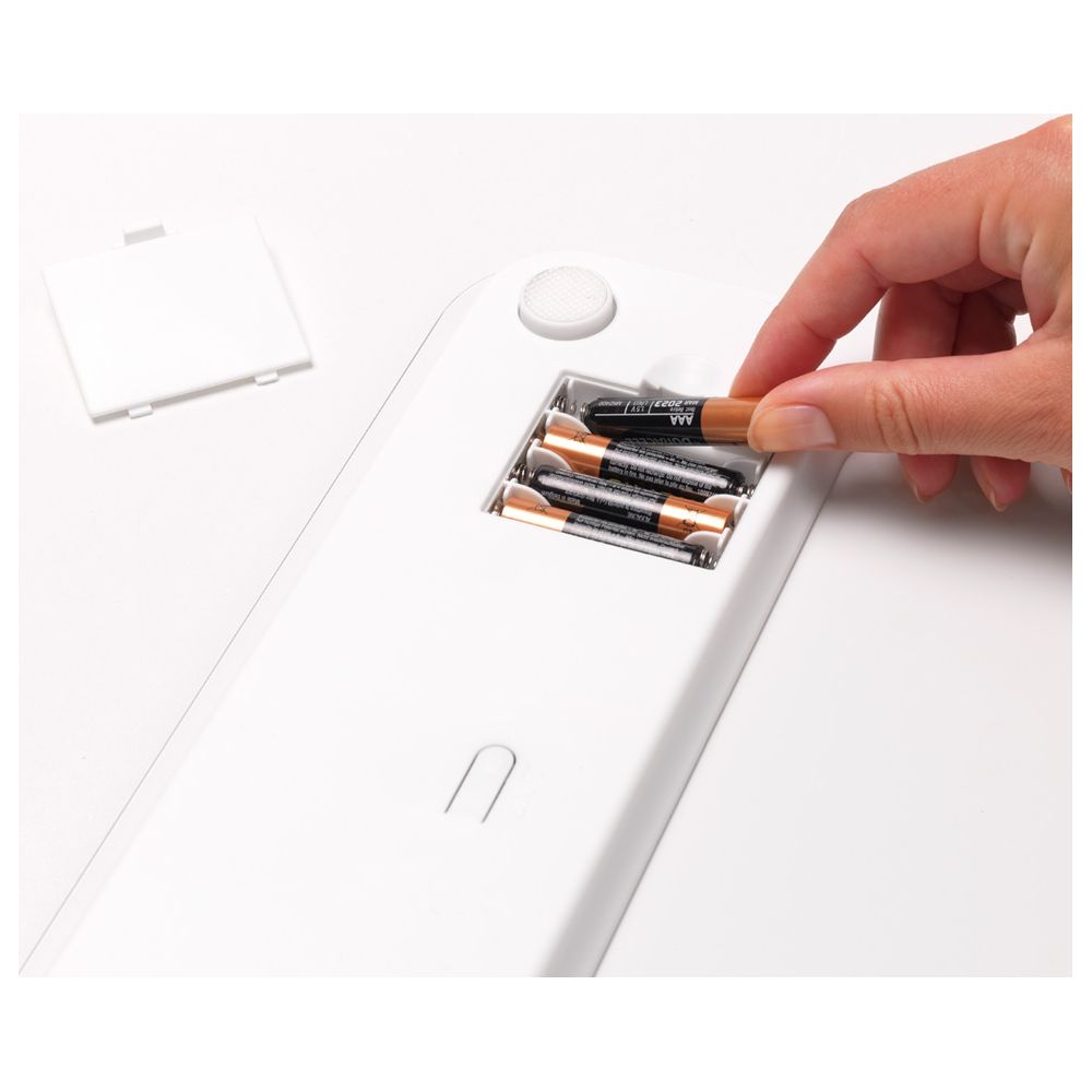 Una mano inserisce una batteria AAA nel vano di un dispositivo bianco.