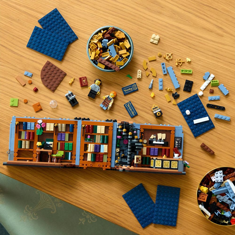 Ahşap bir masa üzerinde Lego tuğlaları, iki minifigür ve kısmen inşa edilmiş bir Lego seti.