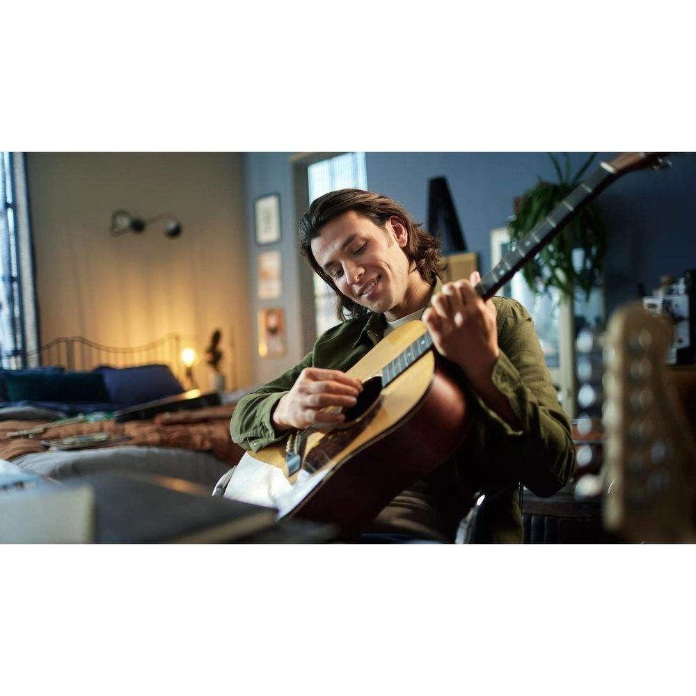Un giovane suona la chitarra acustica in una camera da letto accogliente.
