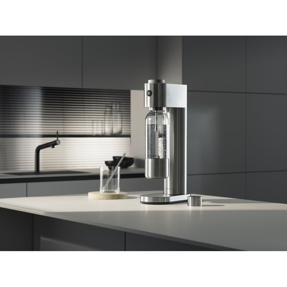 Gasatore d'acqua in acciaio inossidabile su un'isola cucina luminosa con un bicchiere e cucina moderna.