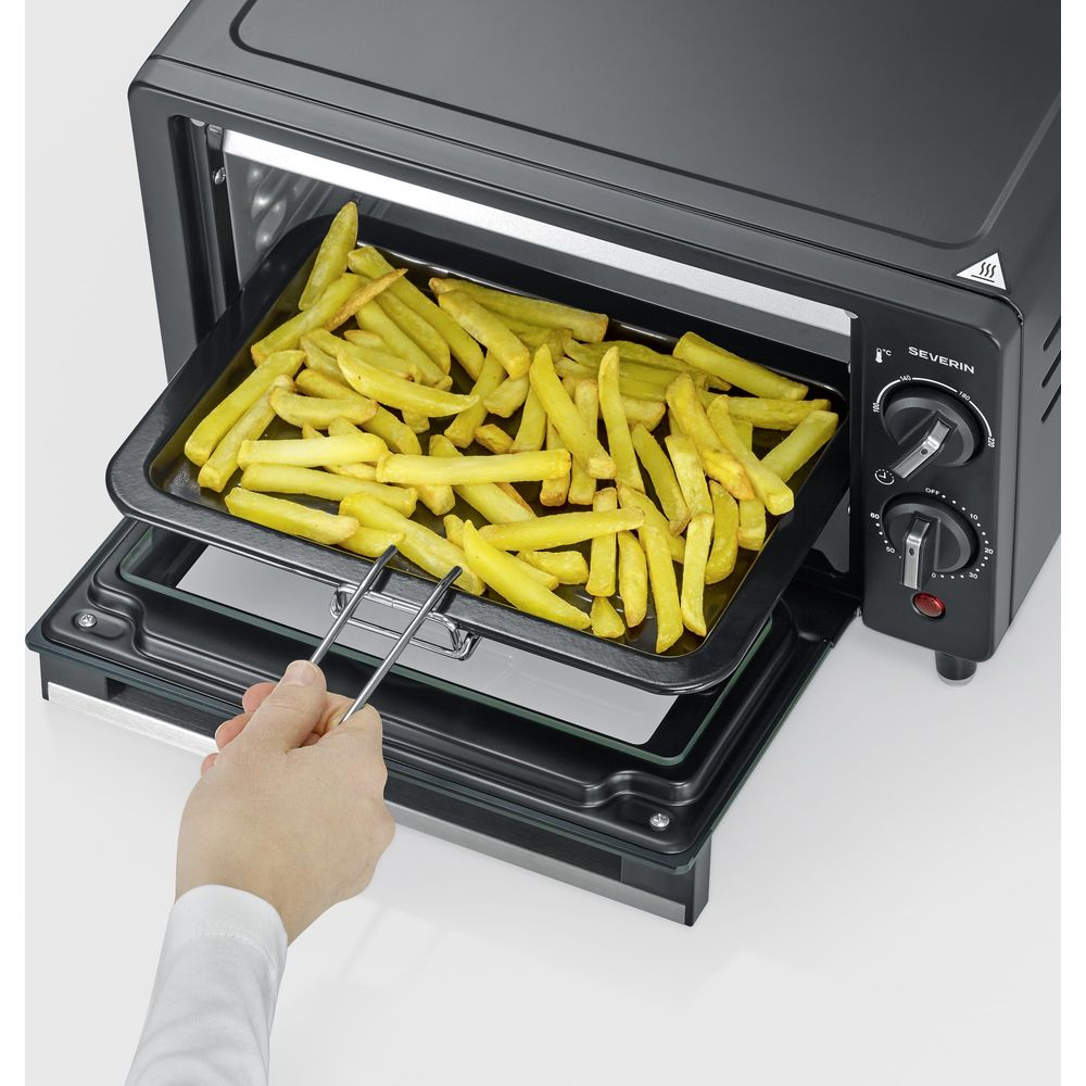 Eine Hand zieht mit einer Zange ein Backblech mit Pommes frites aus einem kleinen schwarzen Ofen.