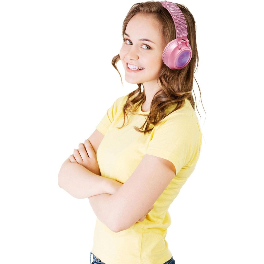 Una mujer sonriente con una camiseta amarilla lleva auriculares rosas brillantes con los brazos cruzados.