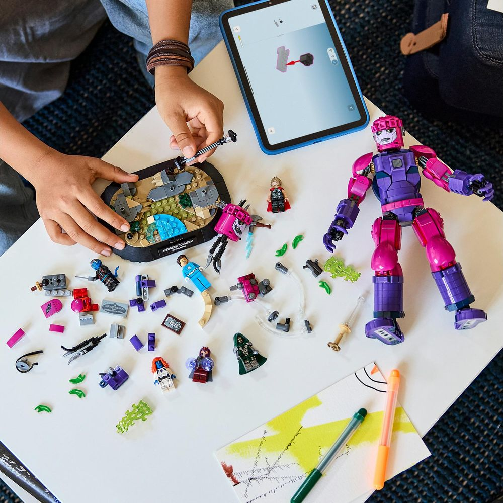 Niño construyendo sets de Lego en una mesa blanca con minifiguras, ladrillos y una tableta.