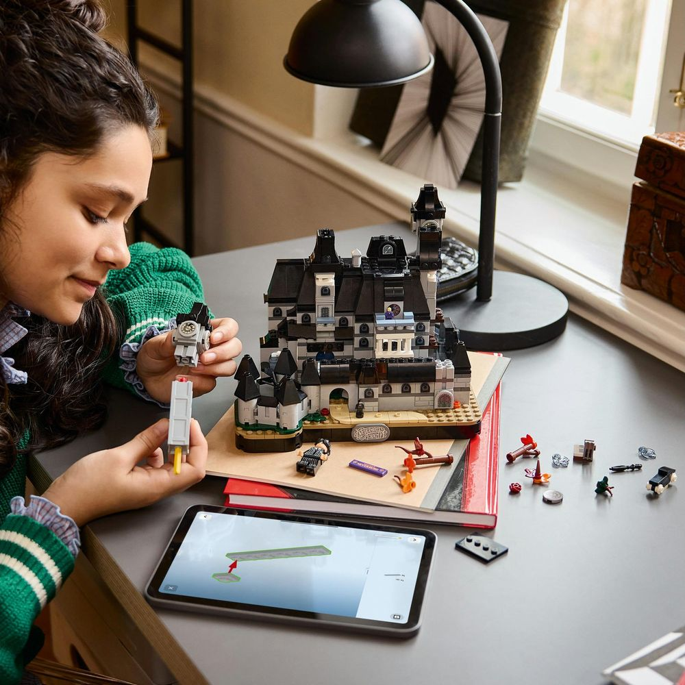 Bir kız, tabletli bir masada büyük siyah bir Lego kalesi inşa ediyor.