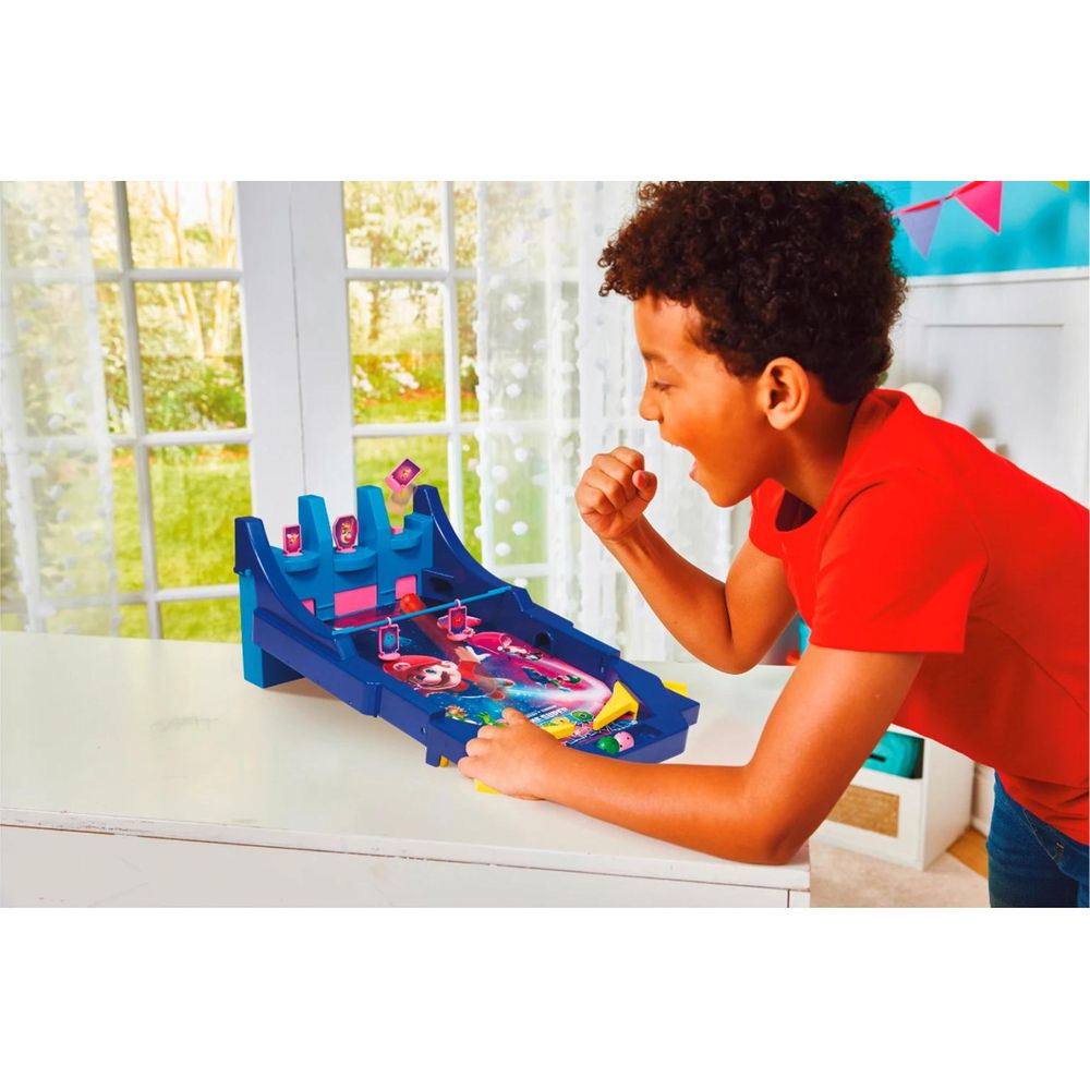 Ein Junge in rotem Shirt jubelt begeistert vor einem blauen Mario-Flipper auf einem weißen Tisch.