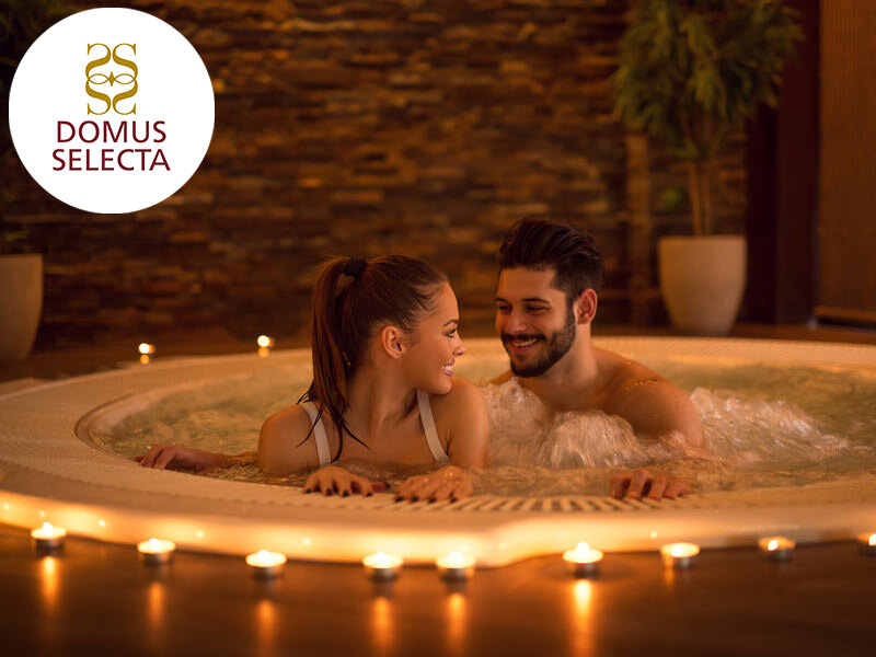 Una pareja feliz se sienta en un jacuzzi rodeado de velas encendidas en una habitación con pared de piedra.