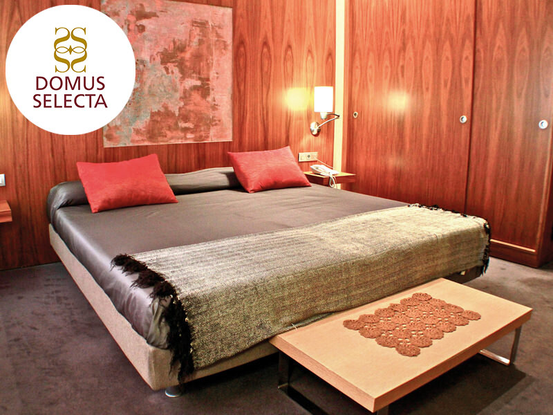 Habitación de hotel lujosa con cama grande, cojines rojos, paneles de madera y un banco.