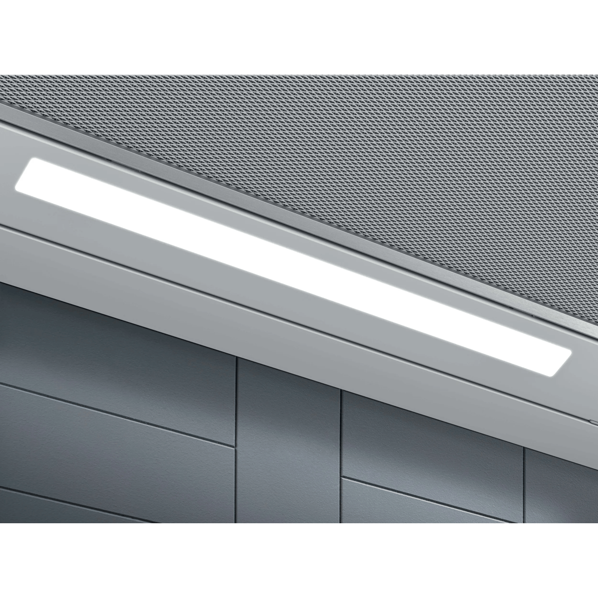 Primer plano de una campana extractora con tira de luz LED brillante, filtro de malla y pared gris.