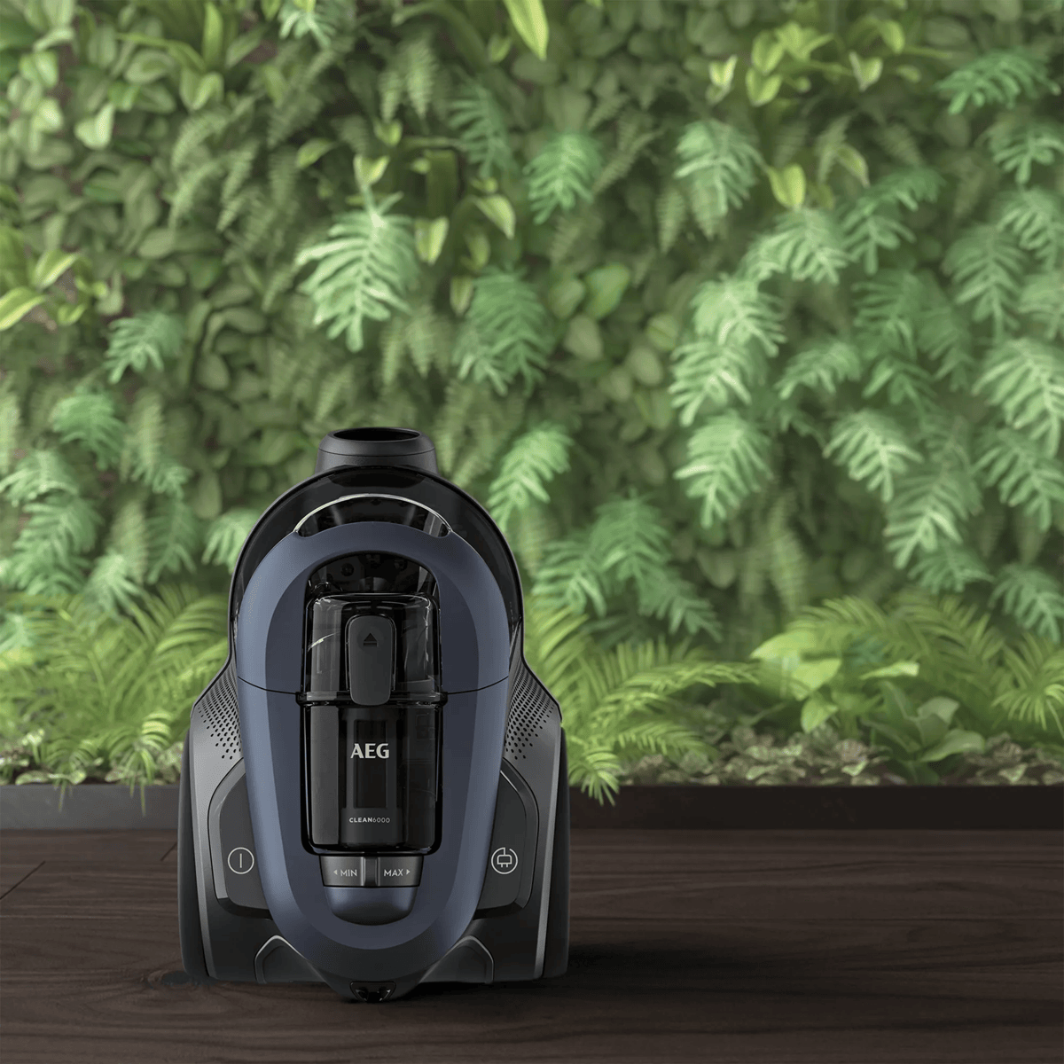 Un aspirapolvere AEG Clean 6000 blu scuro è su un pavimento in legno scuro con sfondo di parete di piante verdi.