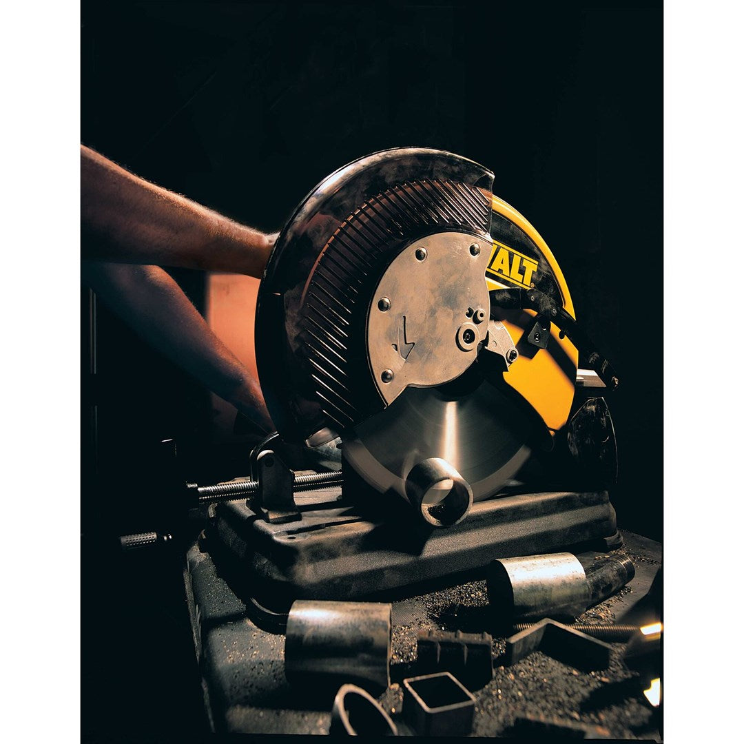 Una persona usando una sierra tronzadora DeWalt amarilla para cortar tubos de metal en un taller oscuro.