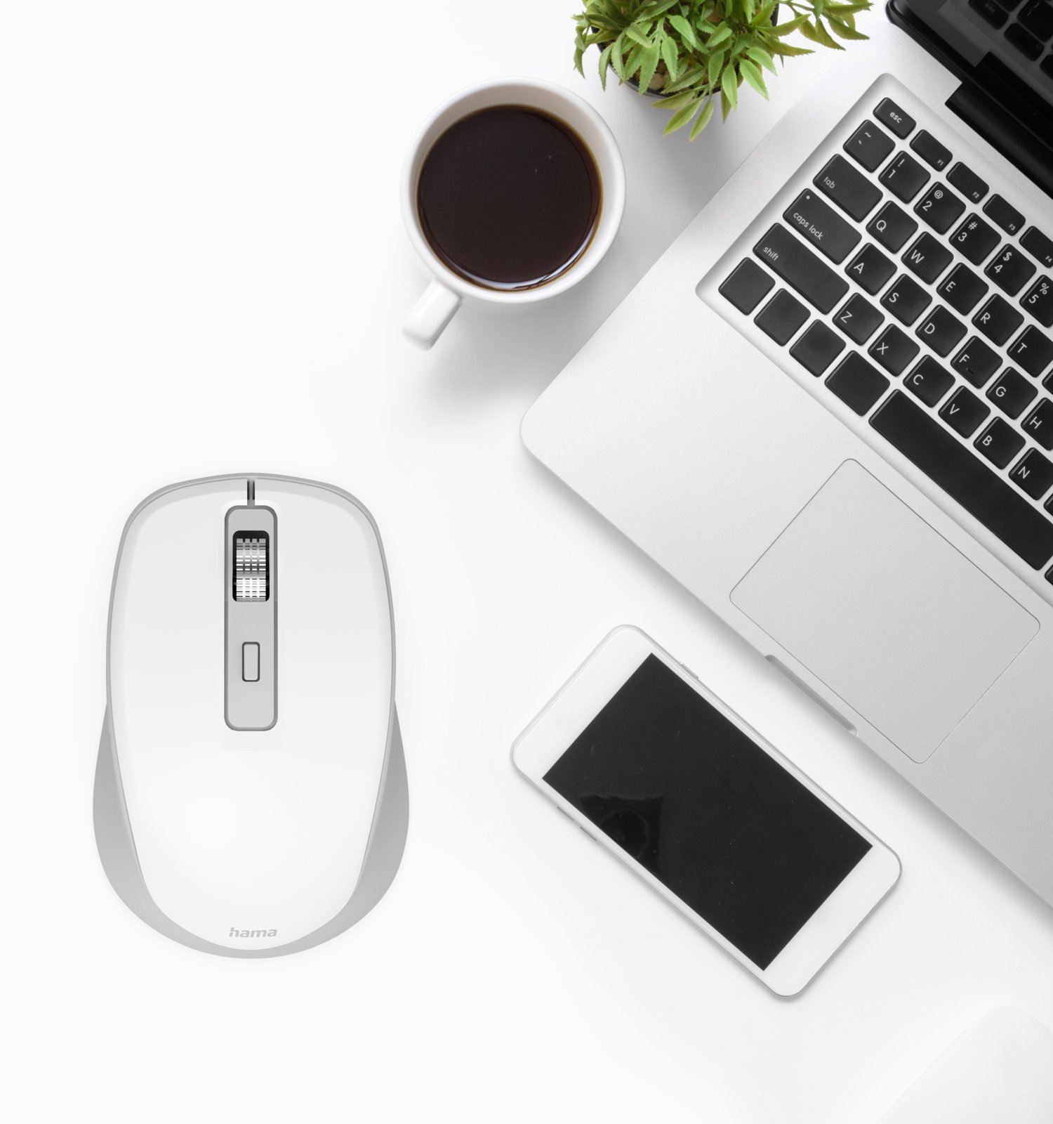 Una scrivania bianca con laptop, mouse, smartphone, tazza di caffè e una piccola pianta in vaso.