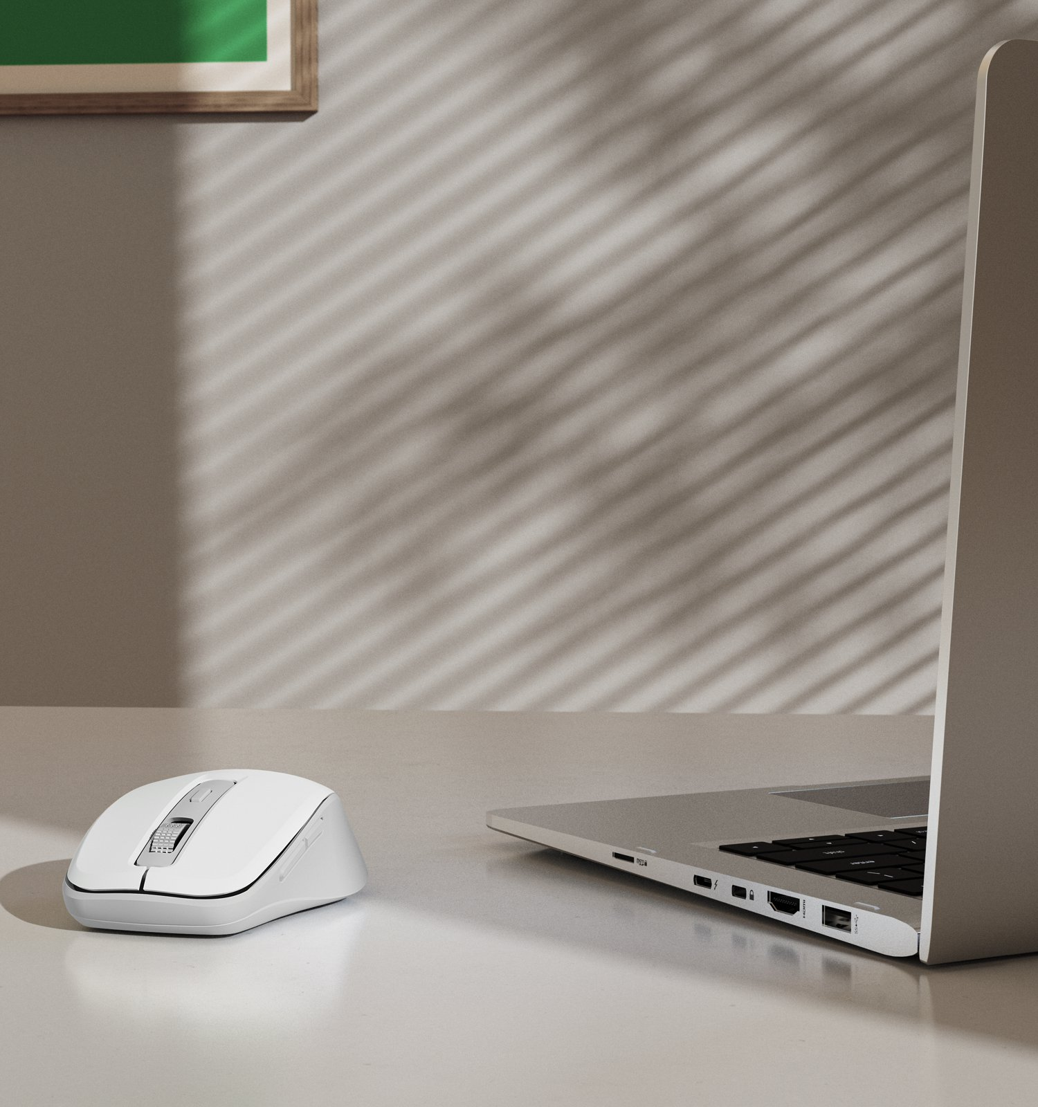 Un mouse wireless bianco e un computer portatile su un tavolo contro una parete con ombre.