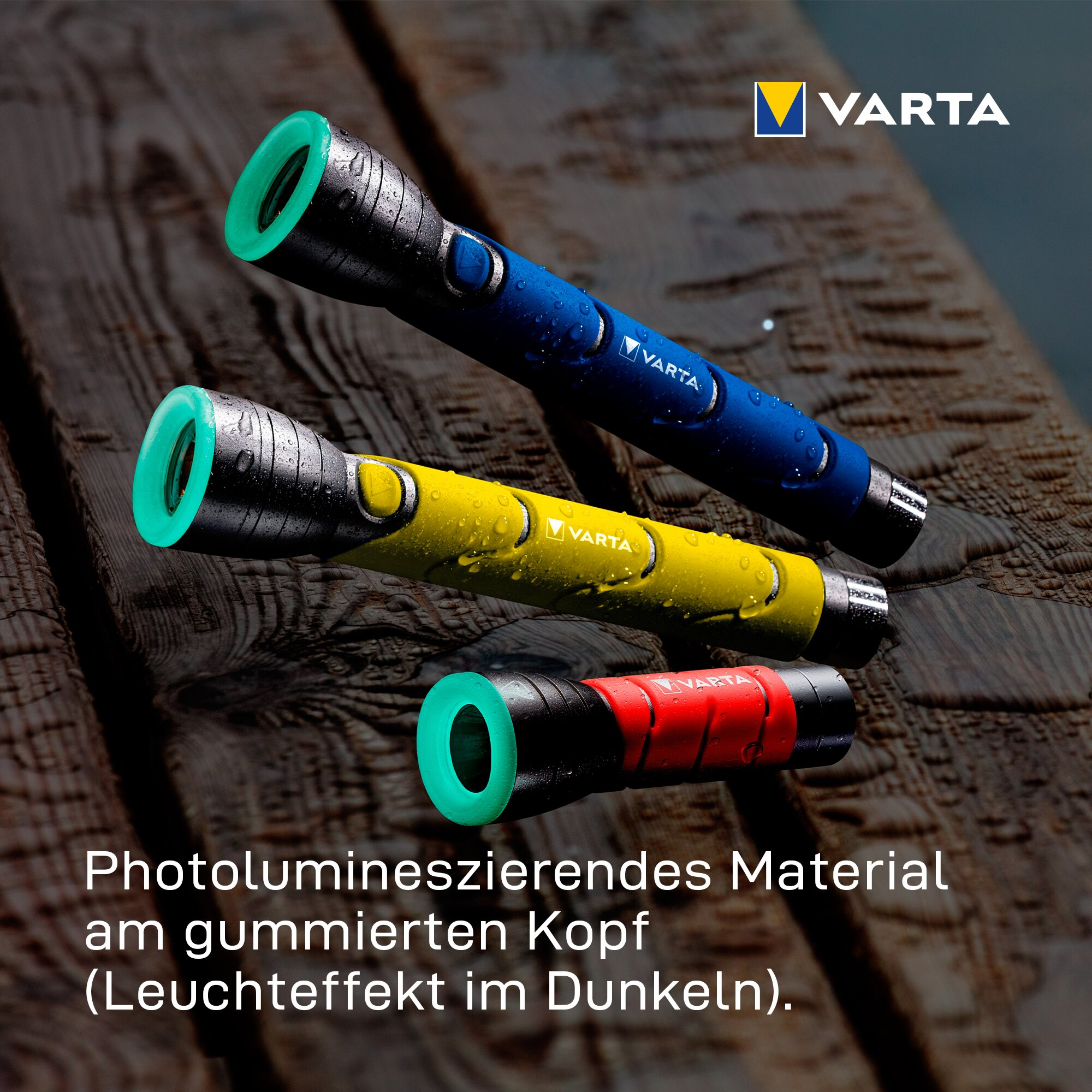 Three Varta flashlights in blue, yellow, and red with glowing green heads on a wet wooden surface.