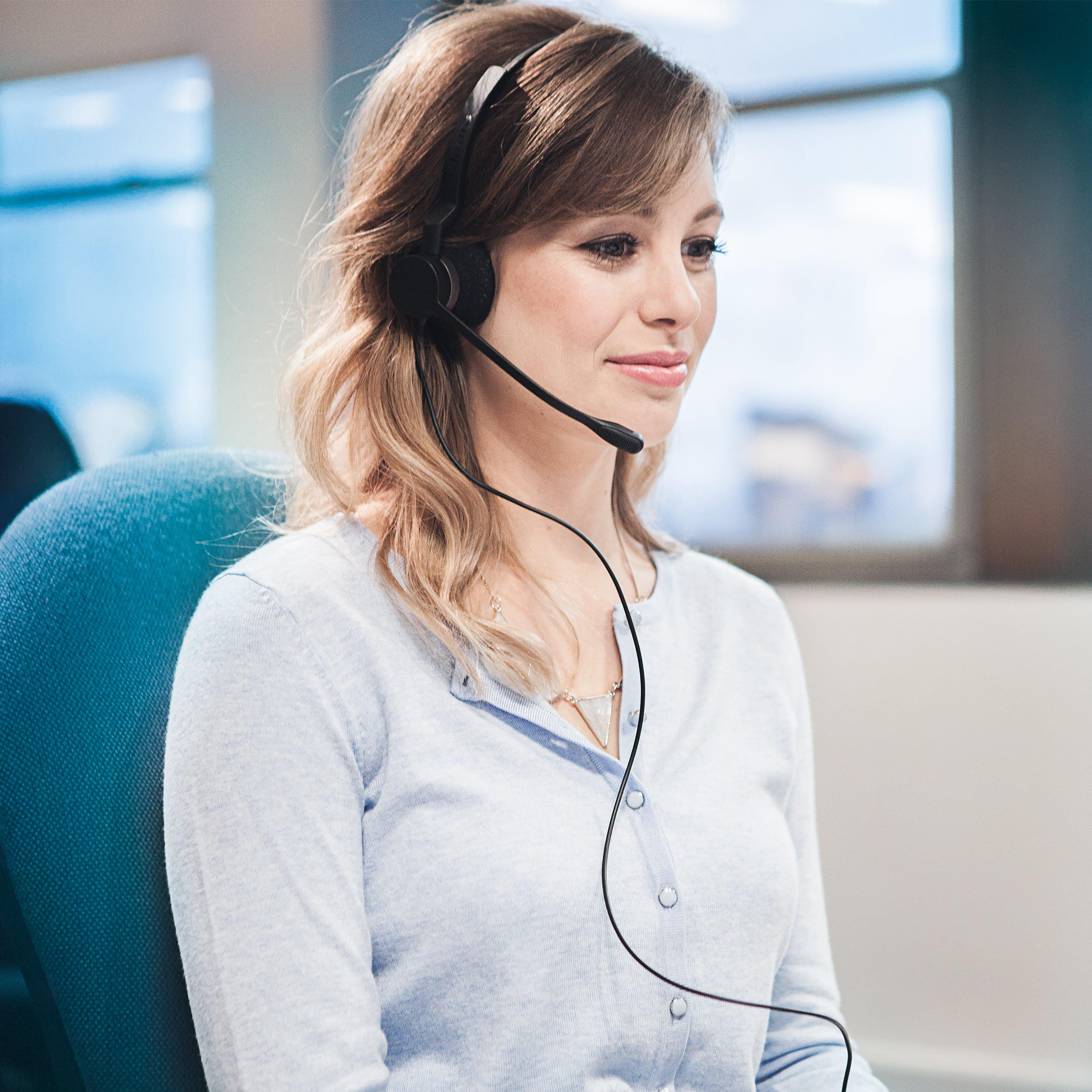 Una mujer con auriculares y top azul está sentada en un escritorio.